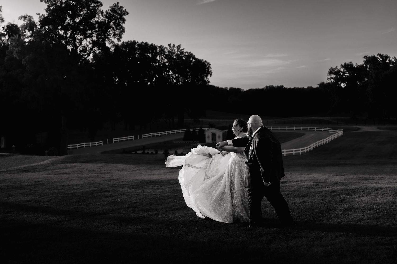 A black and white wedding photo series showing romantic moments on a grassy hill at sunset.