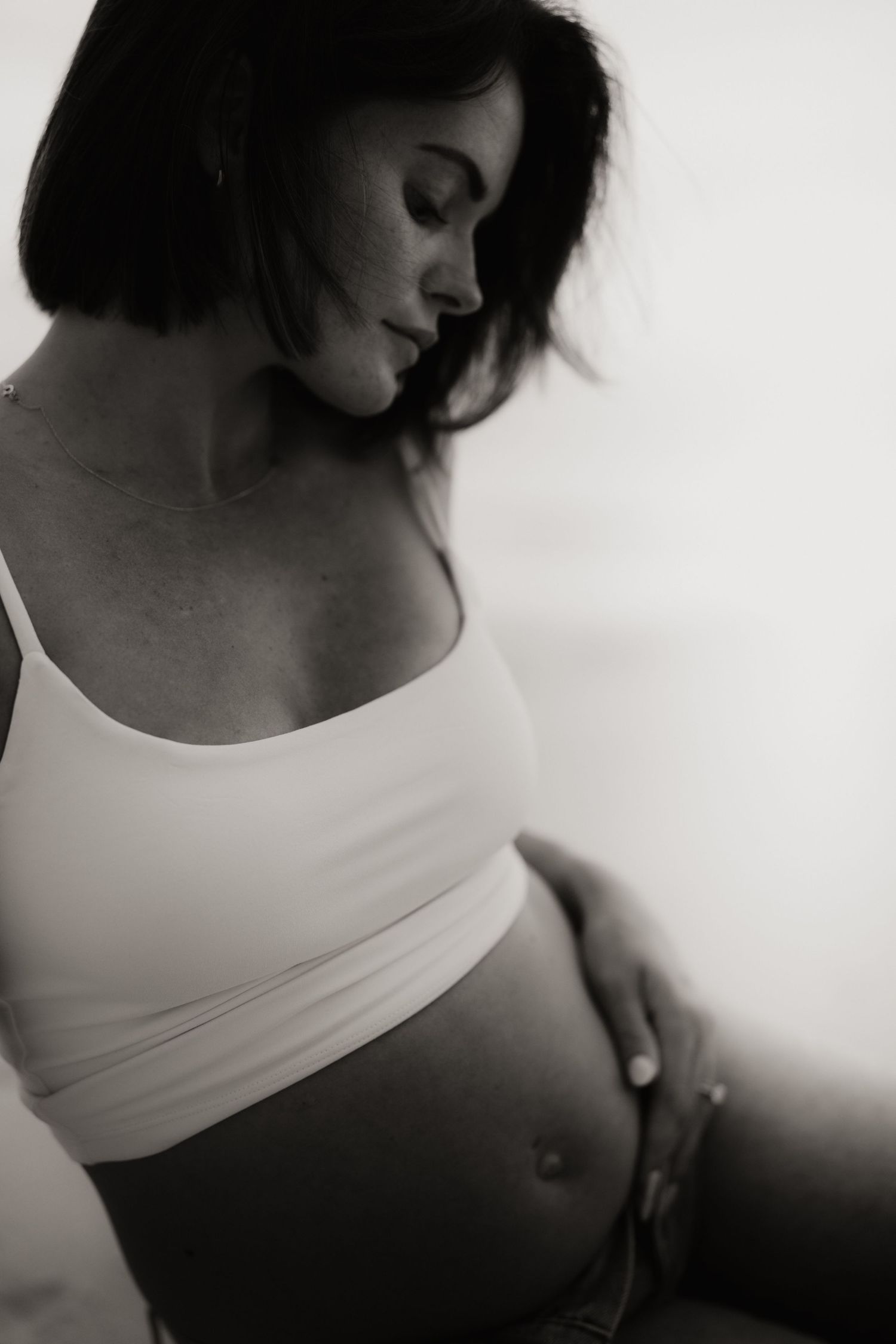 Black and white maternity photo of a pregnant woman in a crop top gently cradling her baby bump.