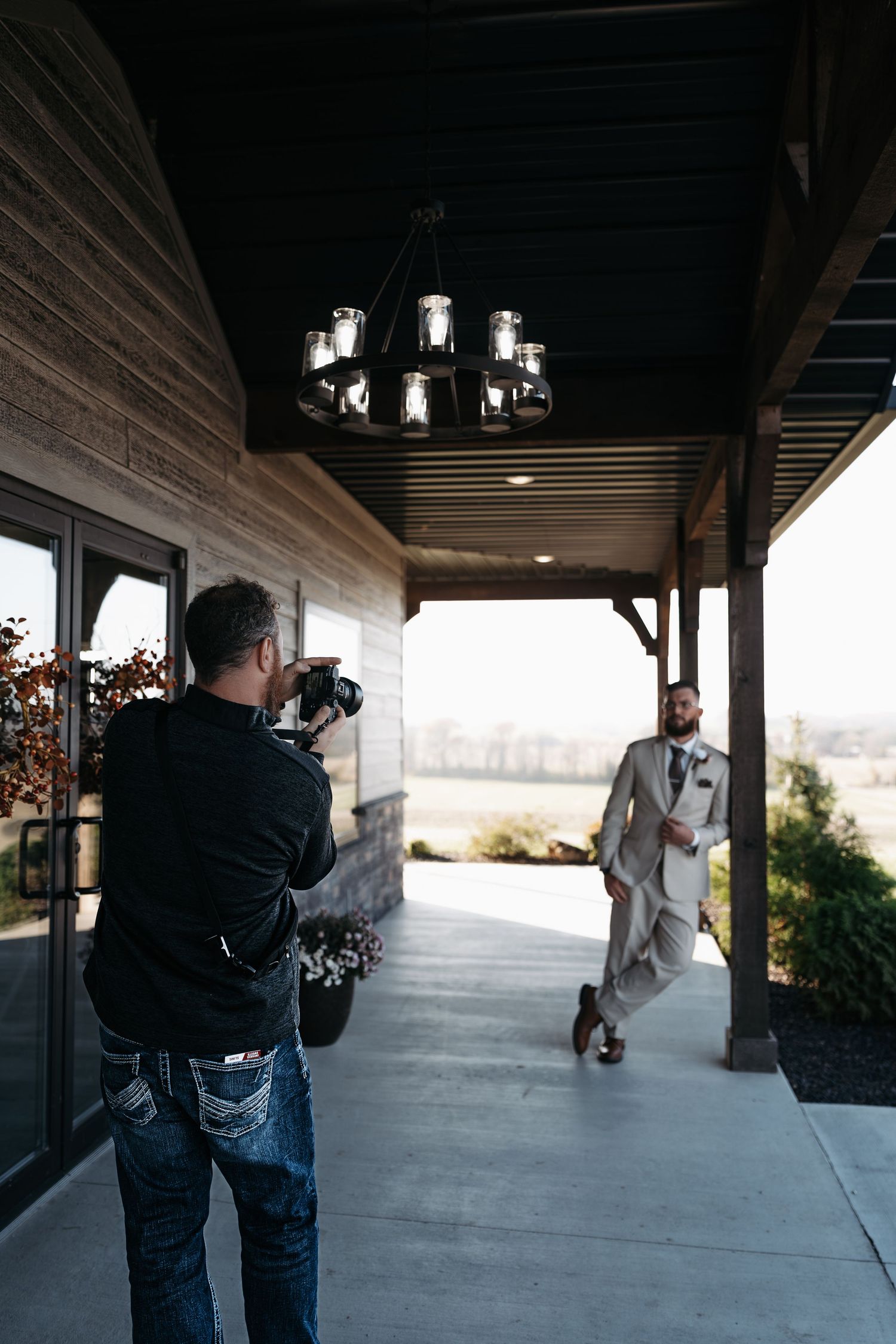Behind the scenes photographer taking pictures of a couple during a wedding photoshoot on a covered porch.