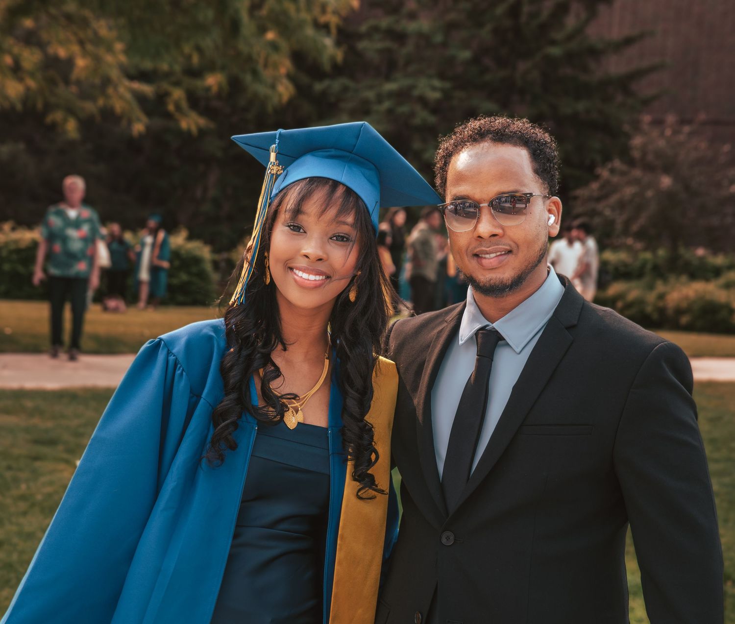 A graduation ceremony photo featuring two people celebrating with one wearing a blue academic cap and gown.