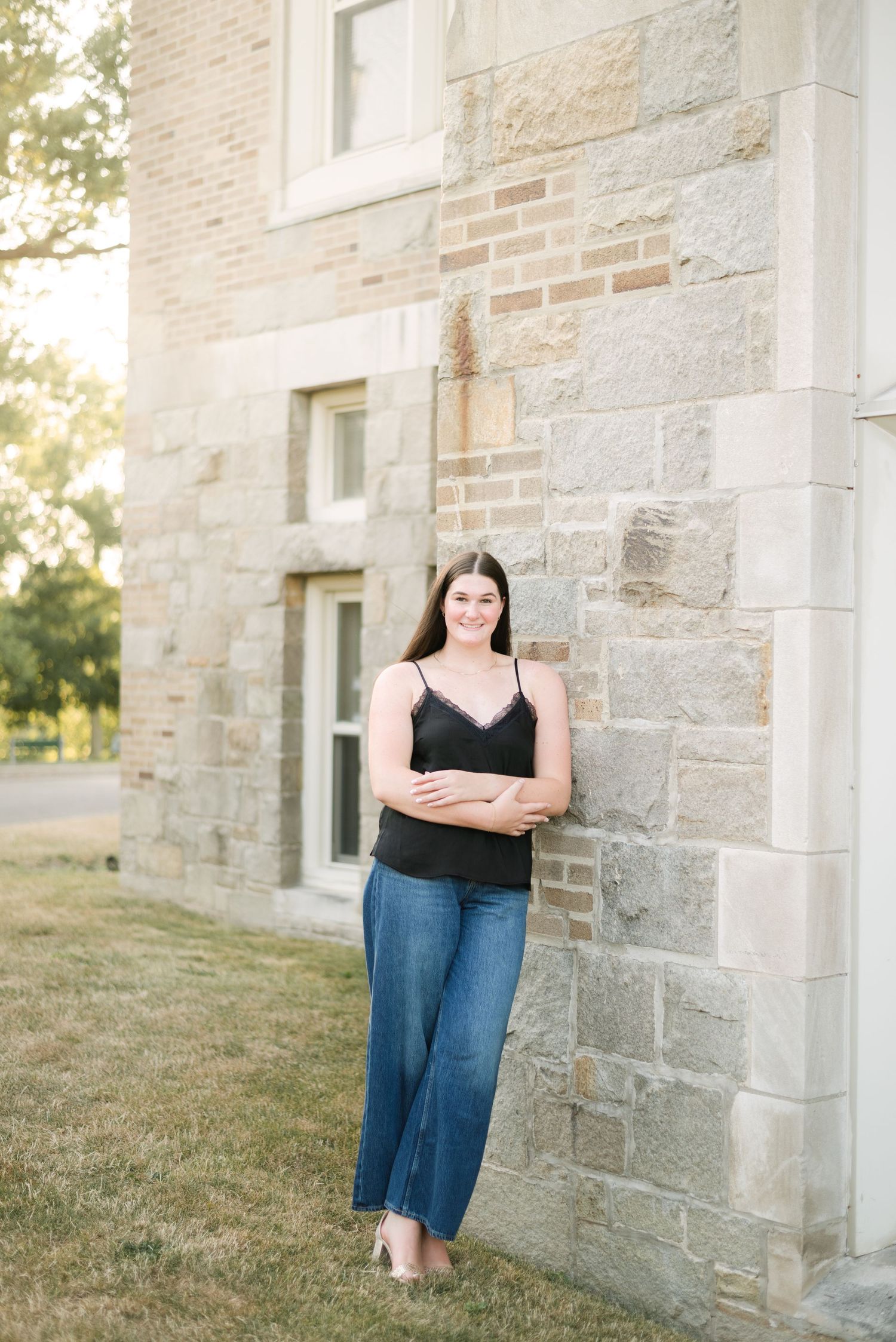 A senior leans against a building during golden hour, wearing a classic outfit.