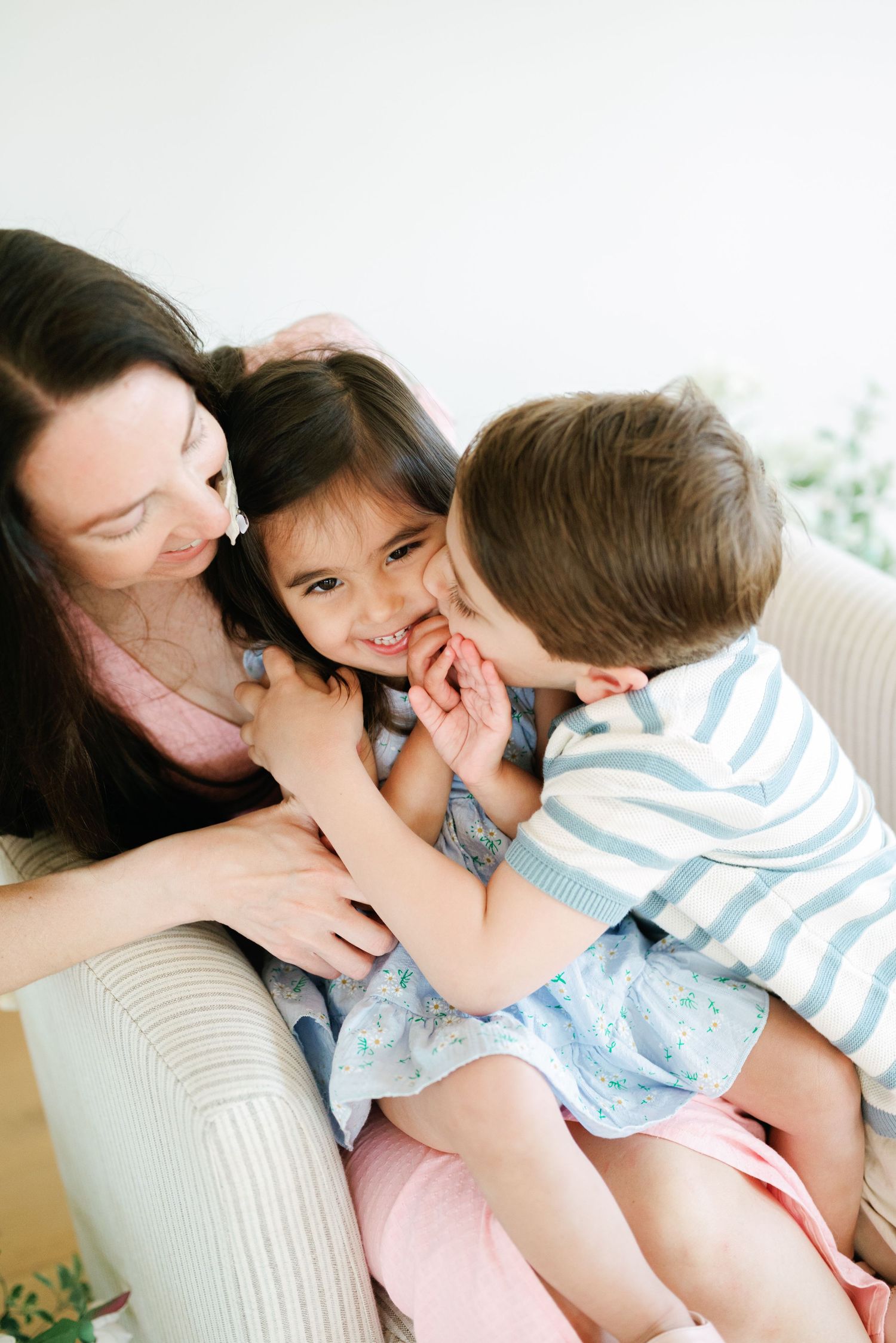 Mom, daughter, and son snuggle on a chair, laughing and smiling.