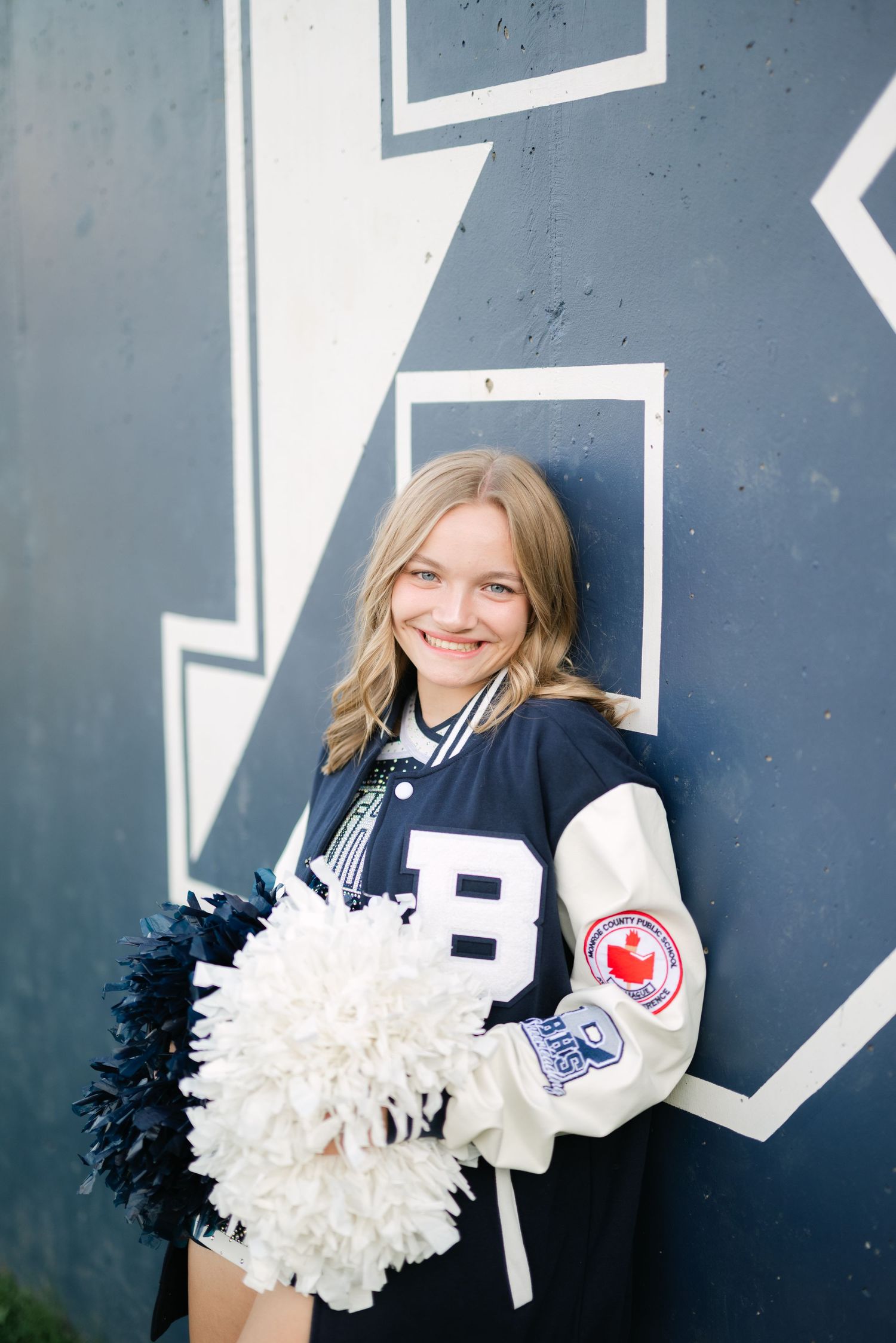 Girl wearing cheerleading uniform and letterman jacket smiling at camera