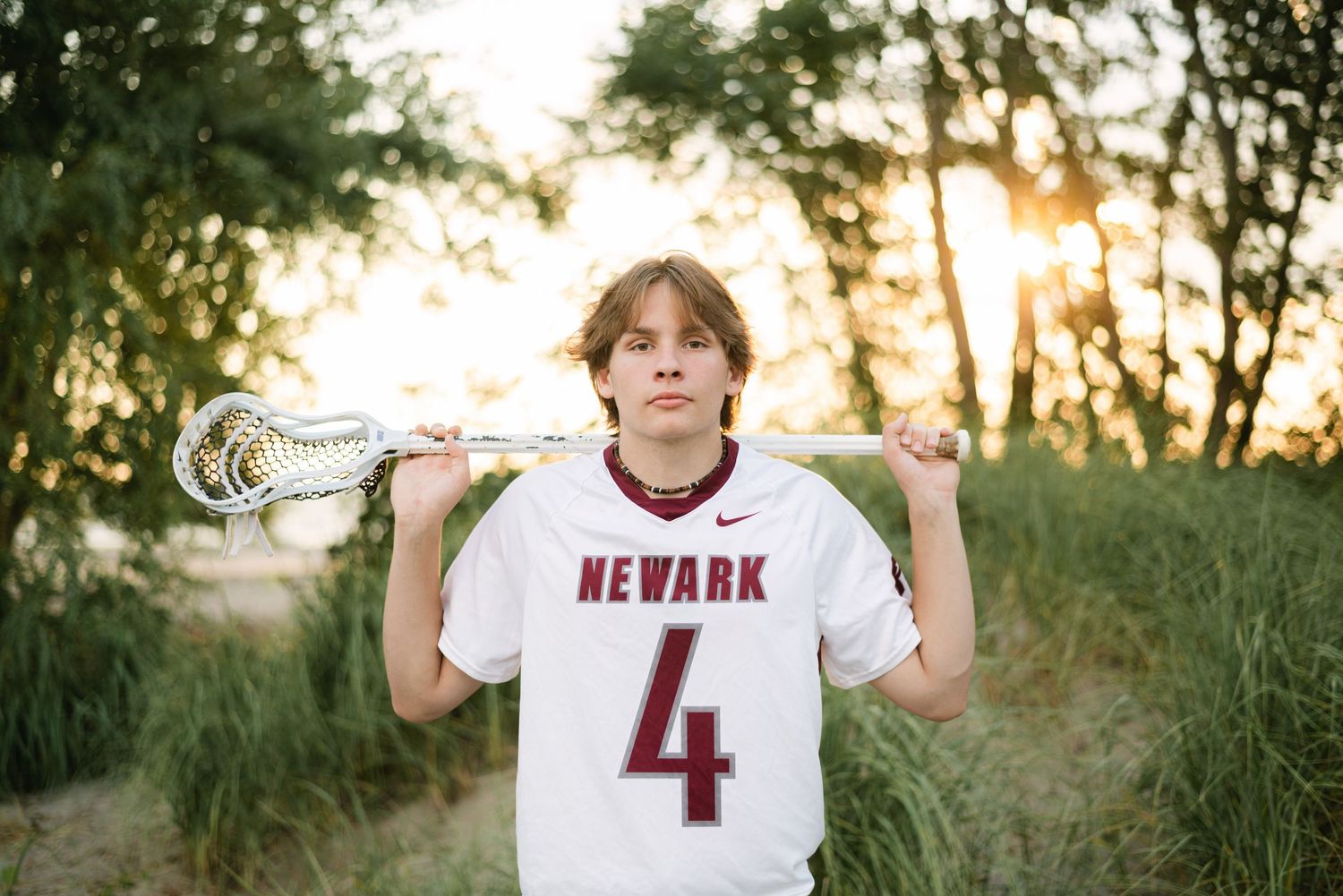 Boy with lacrosse stick over shoulders, looking serious at the beach