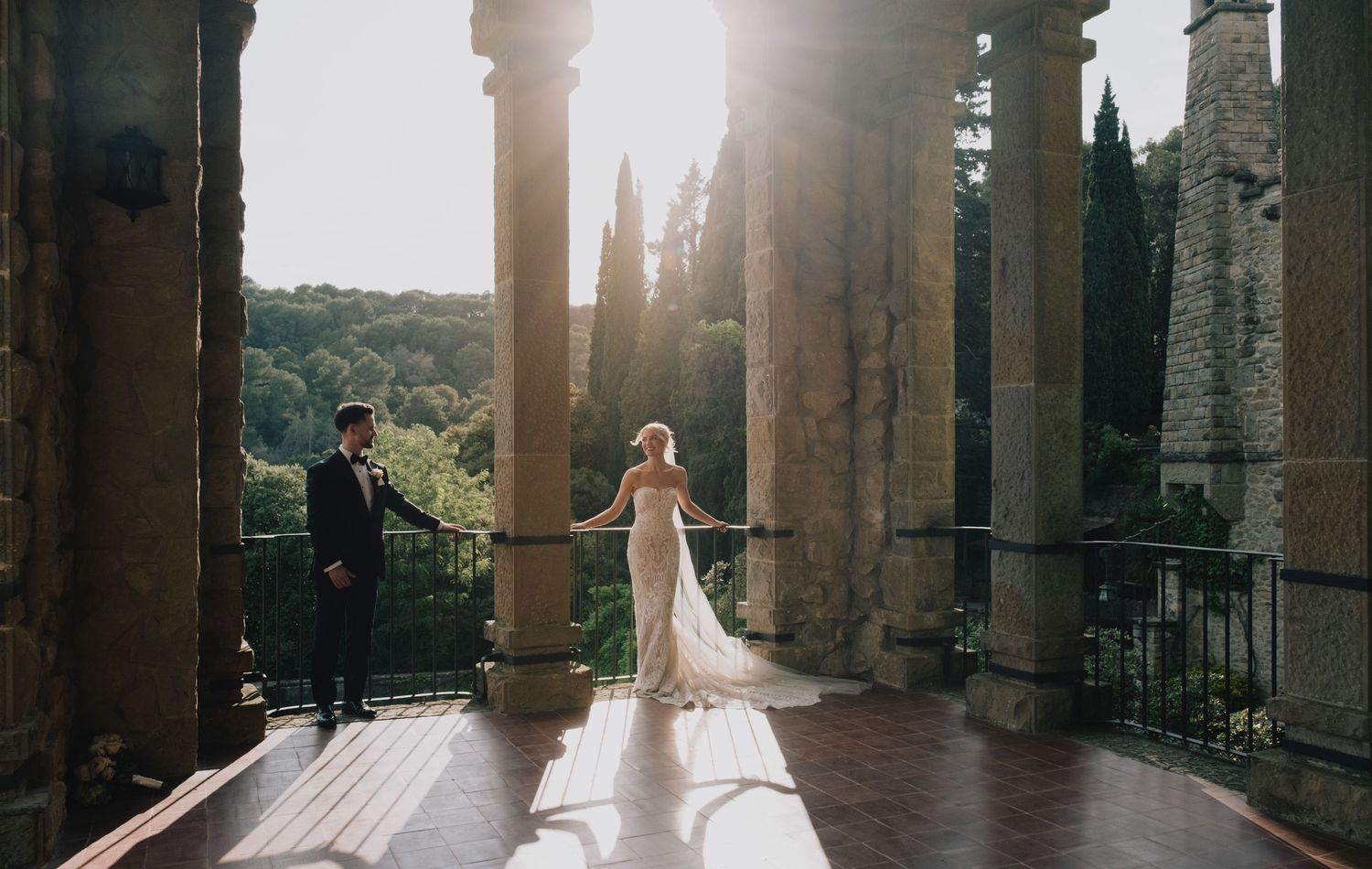 Wedding couple standing in historic archways with dramatic sunlight streaming through.