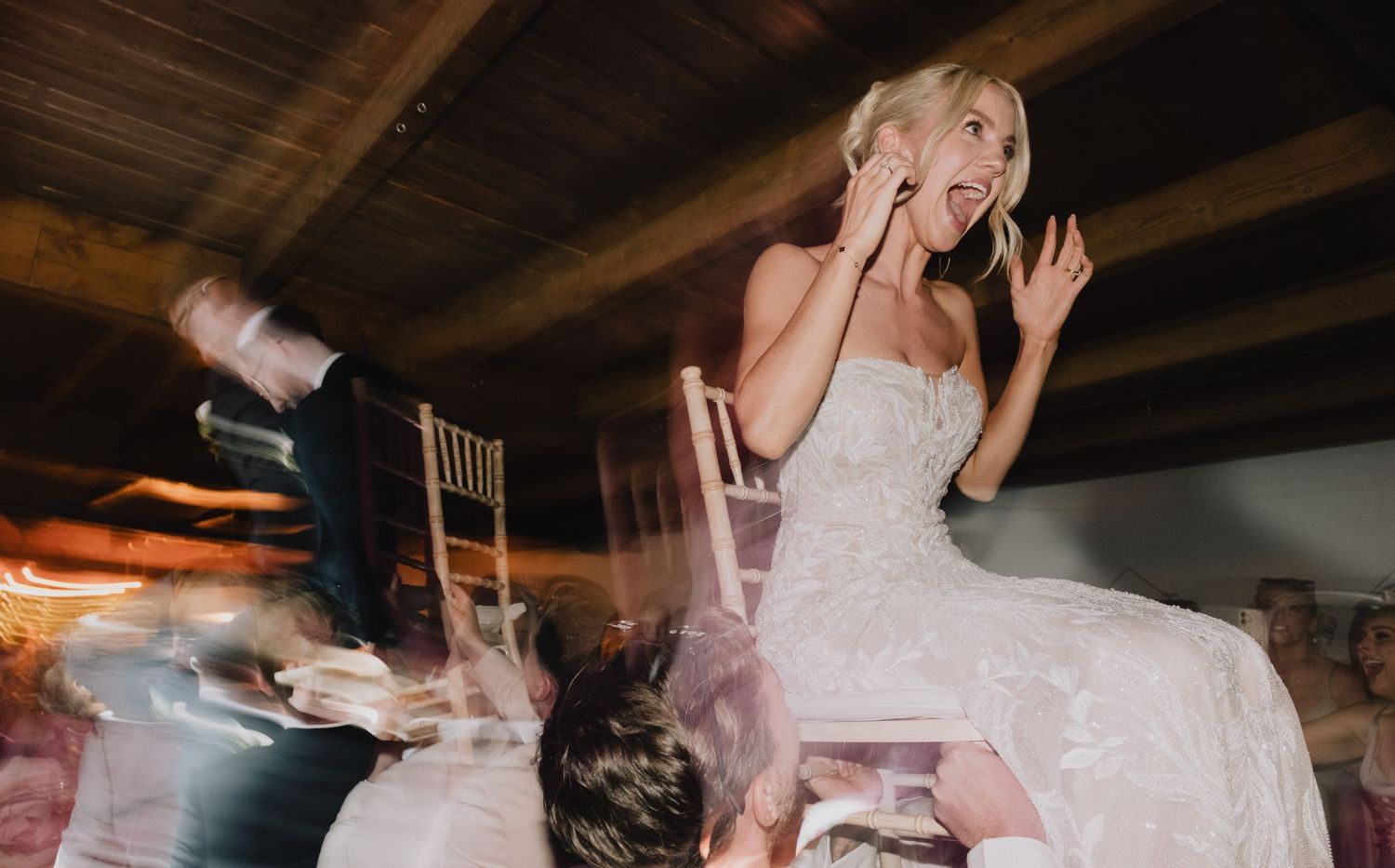 Wedding celebration dance floor moments captured in motion blur under wooden beams.