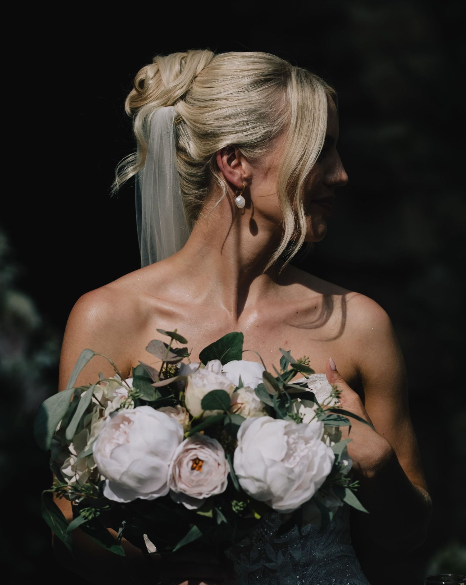 Close-up detail of white roses and greenery in bridal bouquet against dark background.