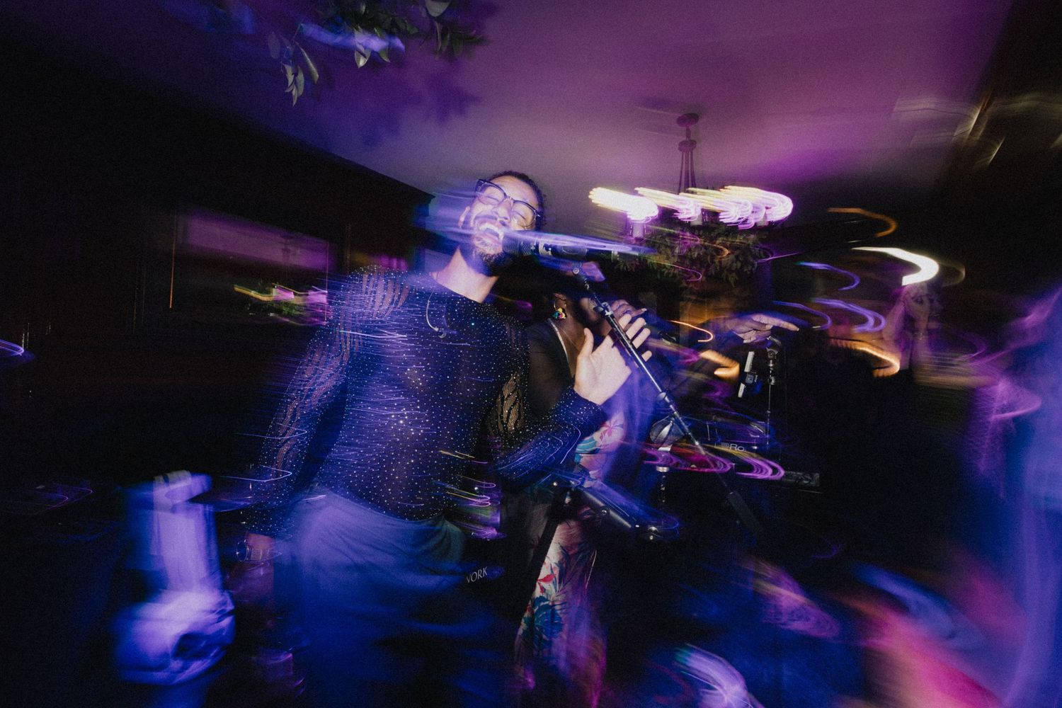 Musician performing on stage with blurred motion effect and purple lighting creating a dynamic concert atmosphere.