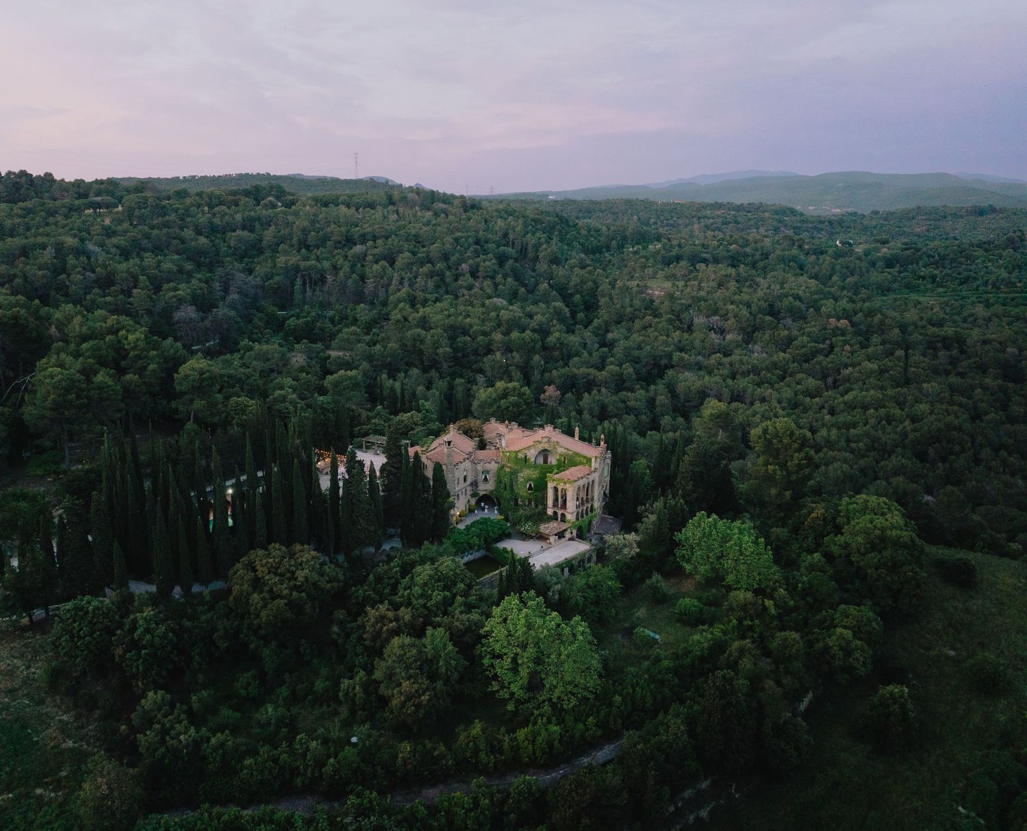 Aerial view of a rustic villa nestled in a forested hillside in Tuscany.