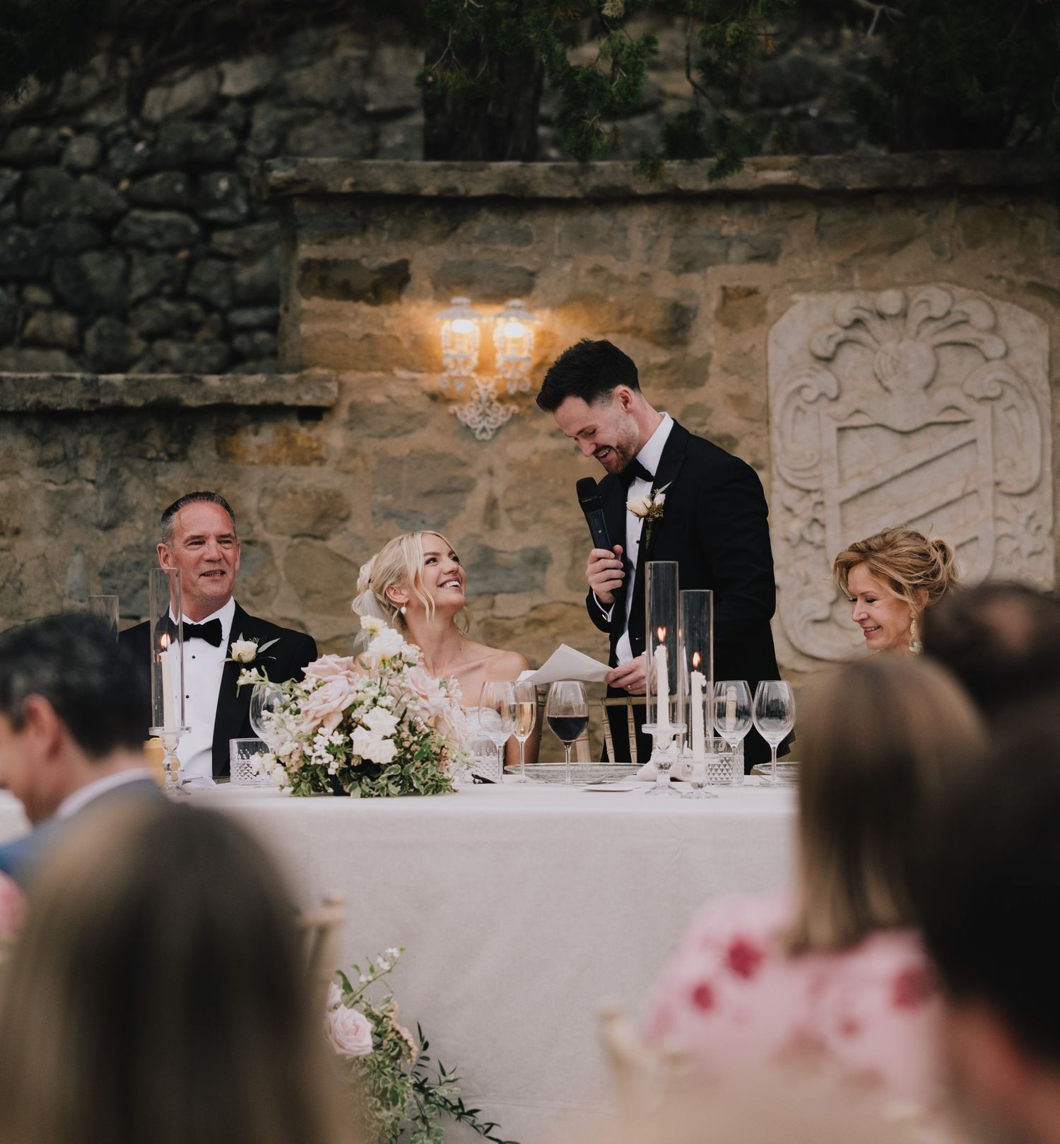 A wedding reception toast at an elegant stone venue with candlelit tables and floral decorations.