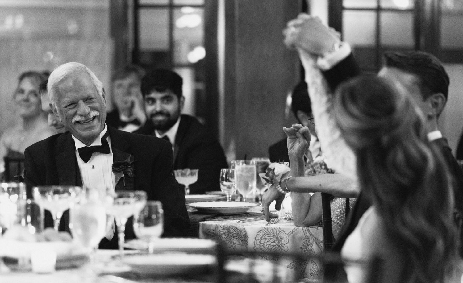 Wedding guests enjoying dinner and conversation at an elegant reception in black and white.