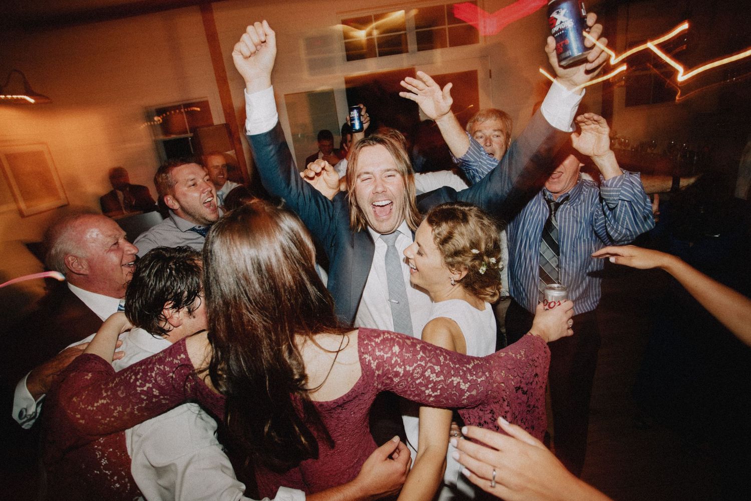 A lively dance party scene at a wedding reception with guests dancing in a dimly lit room.