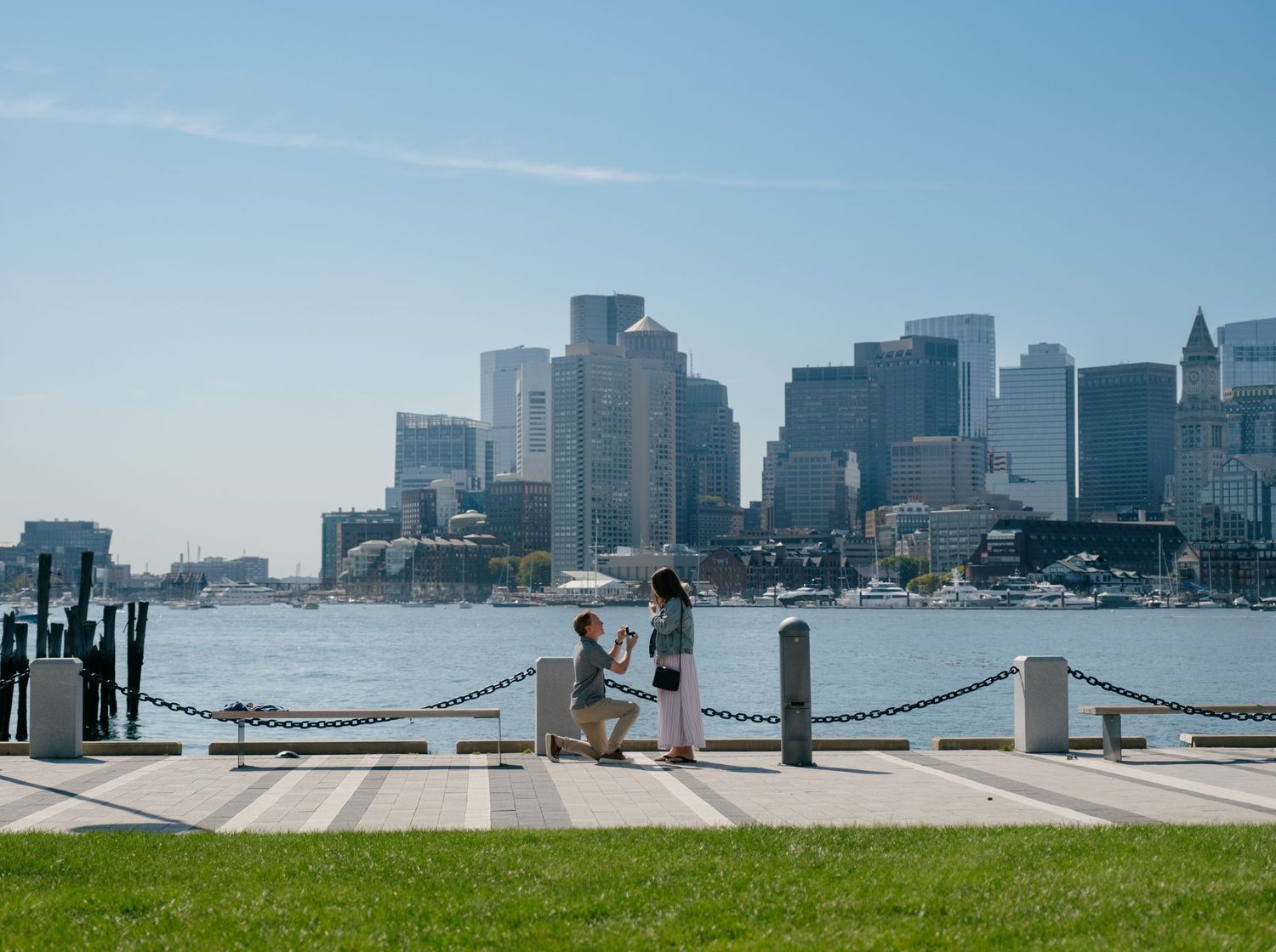 Panoramic view of Boston Harbor waterfront with boats docked at piers and city skyline in the background.