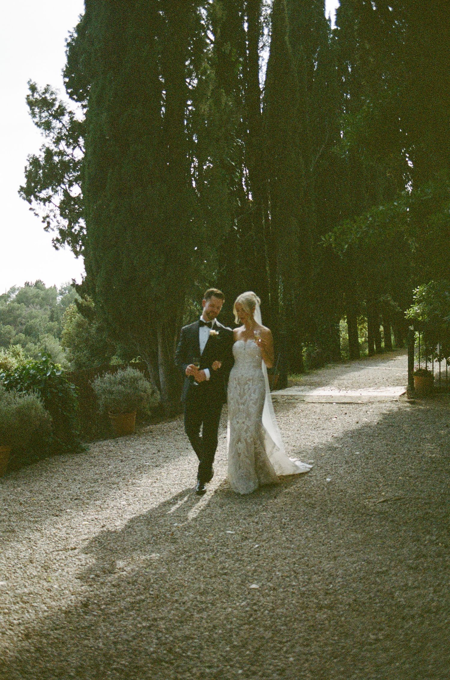 A couple walking along a tree-lined path during their wedding day.