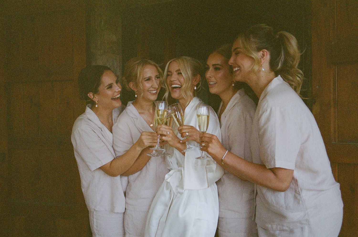 Group in white robes toasting with champagne during wedding preparations.