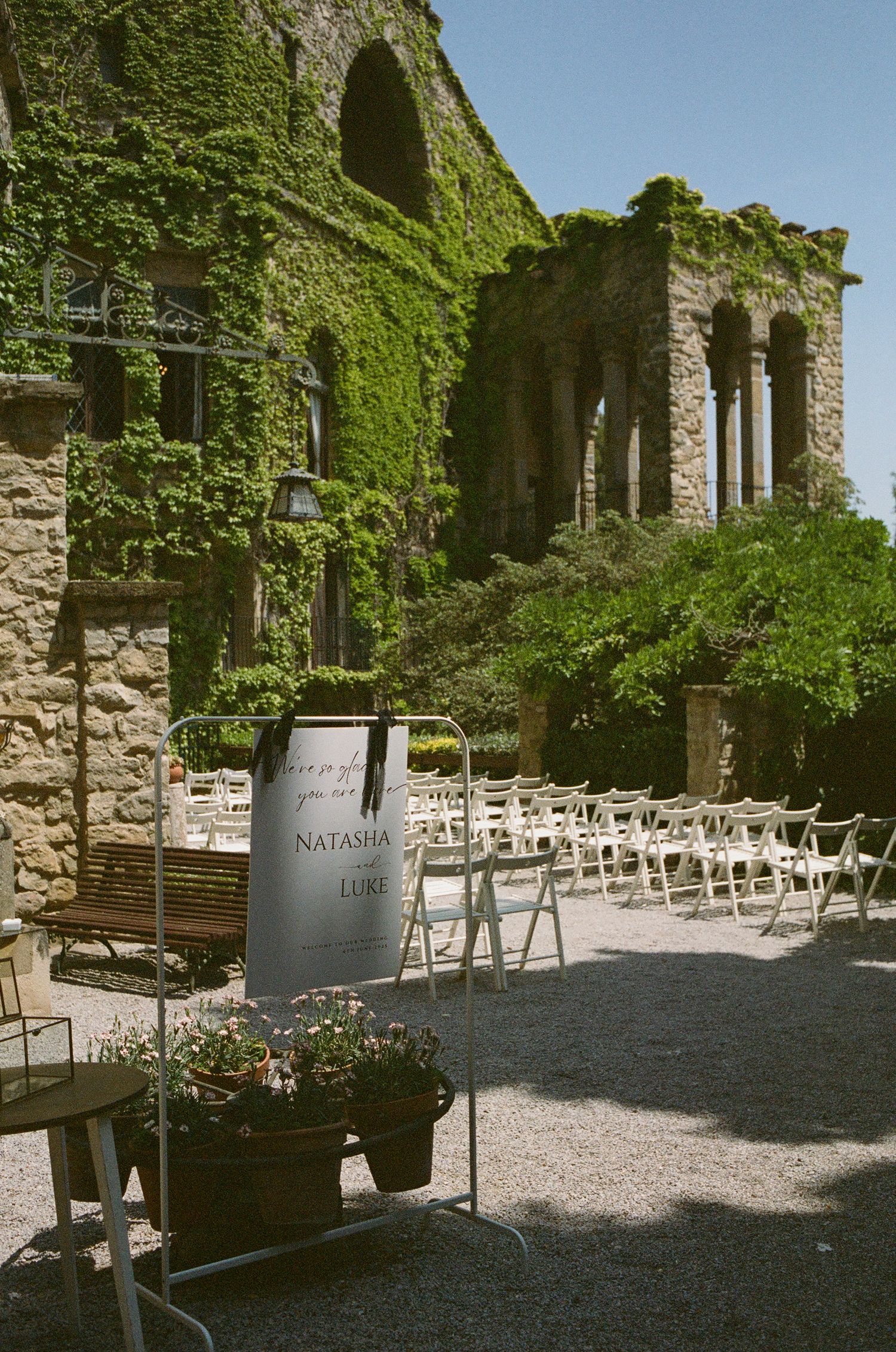 Ivy-covered stone building set up for an outdoor wedding ceremony with white chairs.