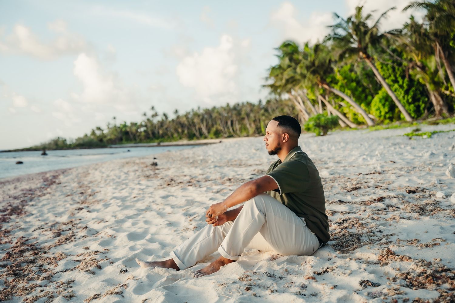 Couple sitting together on a tropical beach at sunset with palm trees in the background.