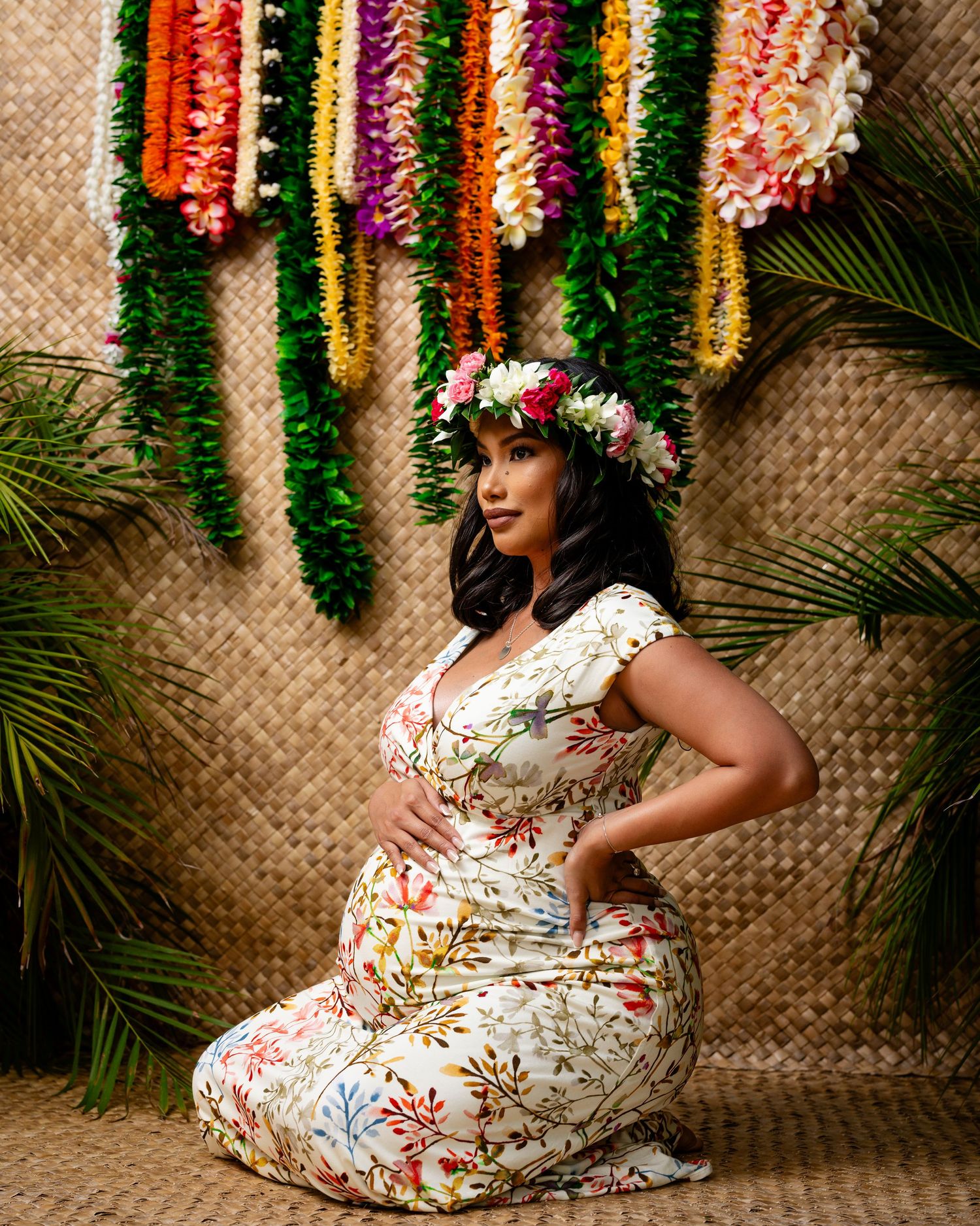 A tropical-themed photoshoot area with colorful floral leis and palm fronds hanging against a woven bamboo backdrop.