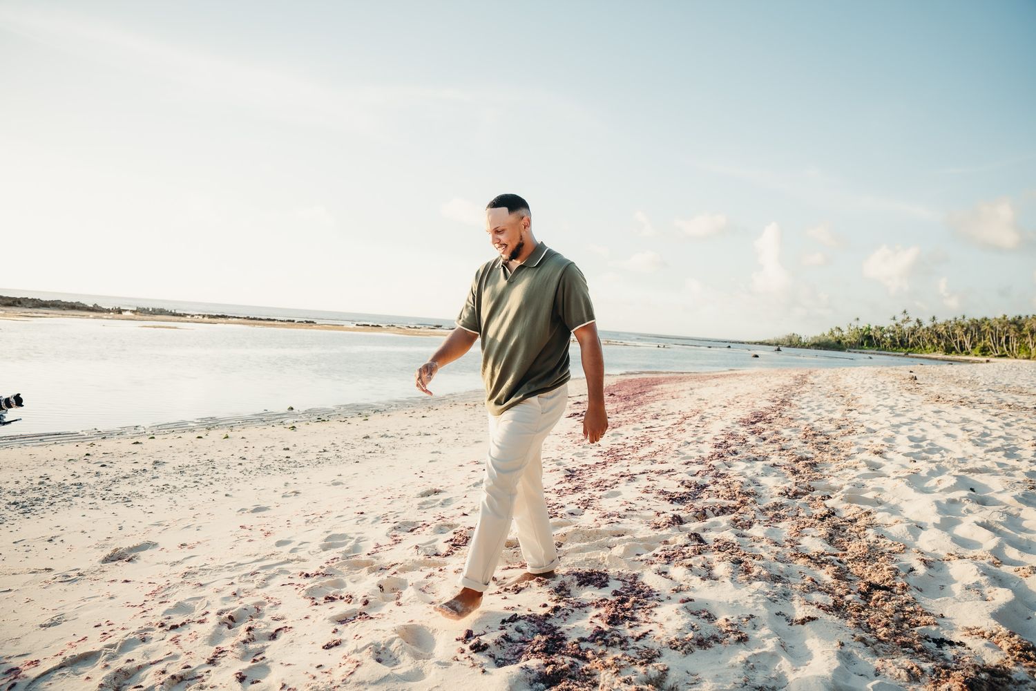 Person walking along a sandy beach shore during golden hour.
