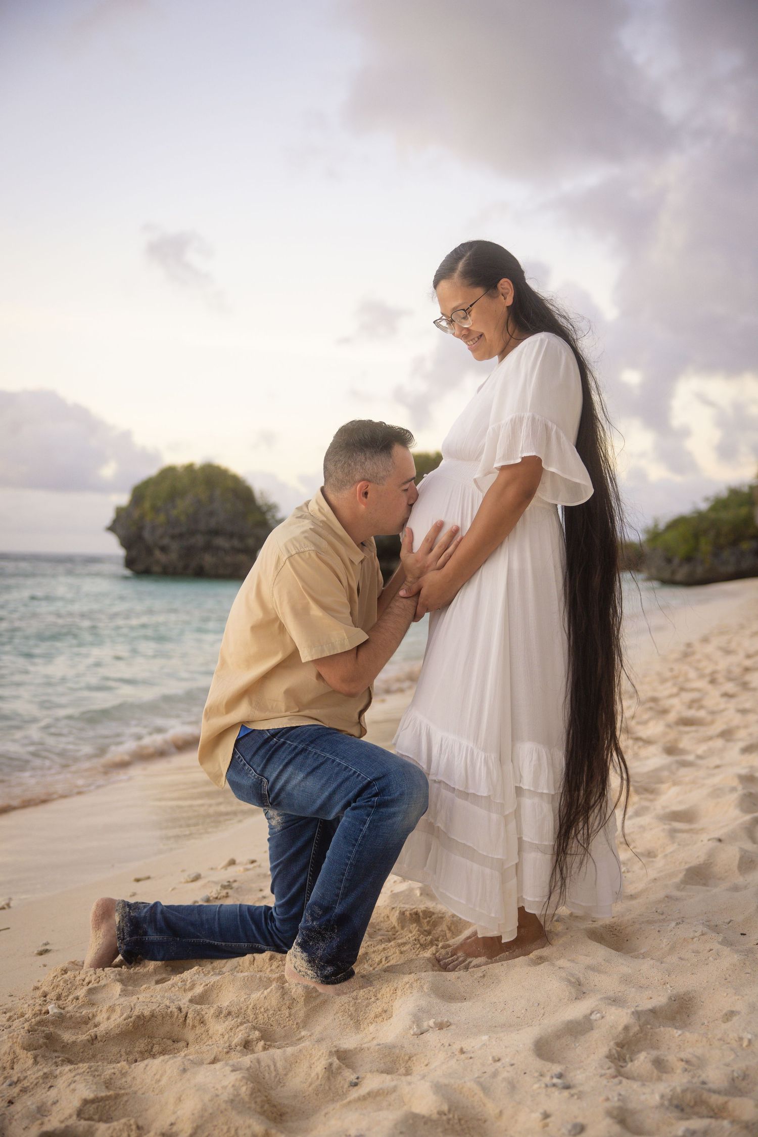 Romantic beach maternity photos with ocean backdrop and cloudy sunset sky.