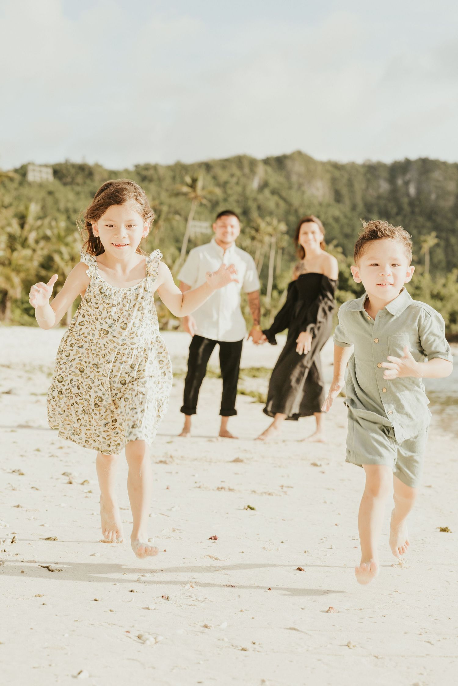 Children running playfully on a beach while adults watch from behind.