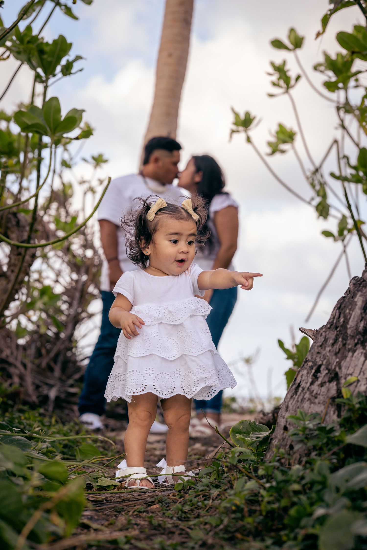 Small child in white dress points excitedly while exploring tropical scenery.