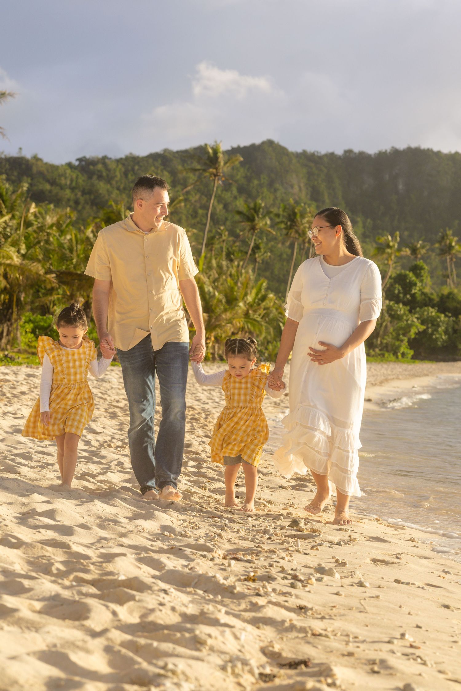 A family takes a stroll together on a sunny beach with mountains in the background.