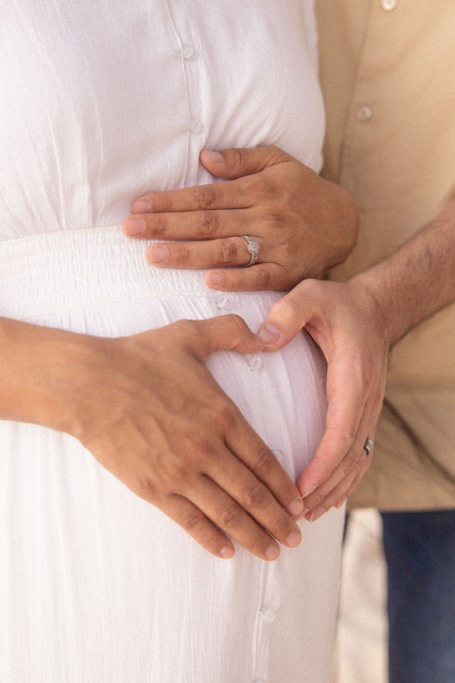 Close-up series of hands gently cradling a pregnant belly in white clothing.