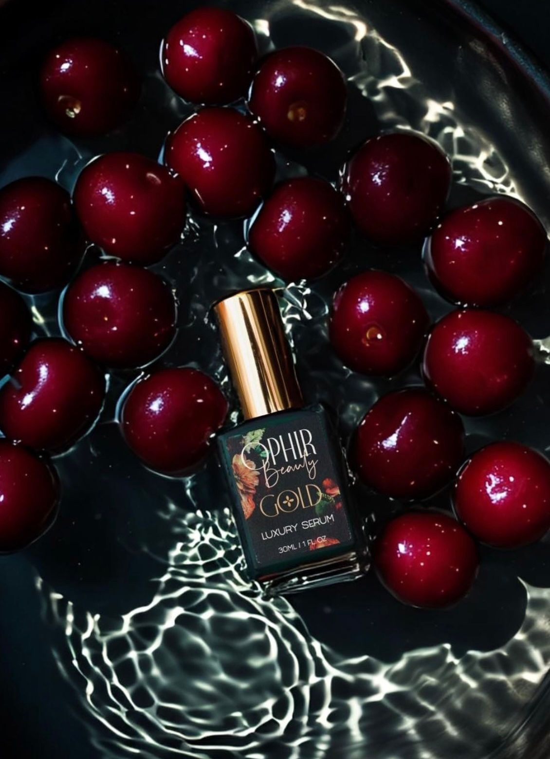 A bottle of Ophir Gold serum splashes into water with cherries floating all around