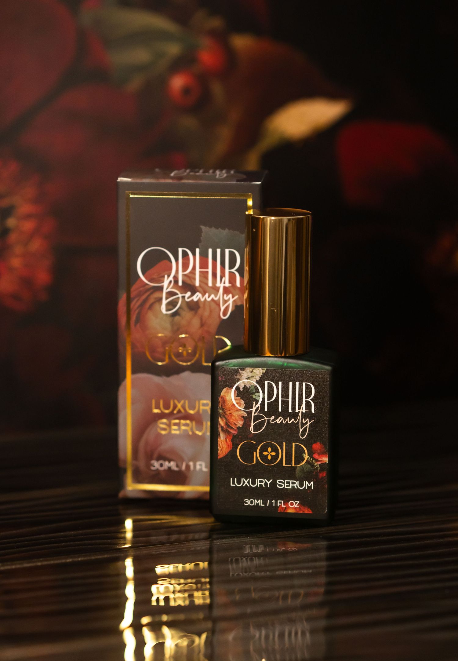 a bottle of Ophir Gold luxury serum stands on a dark reflective surface with deep florals in the background