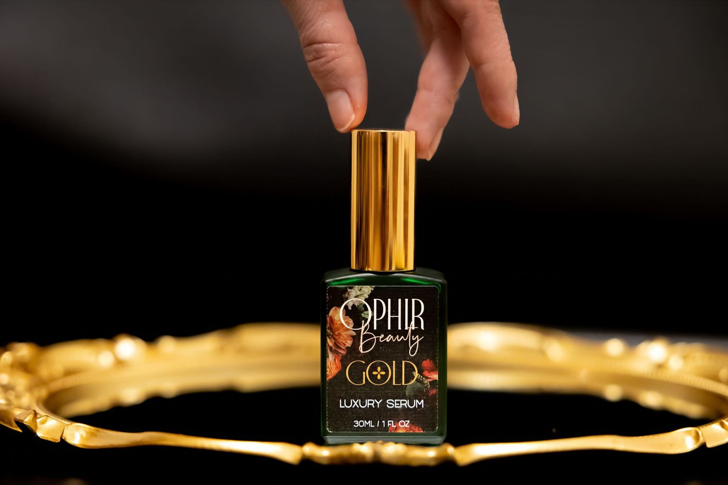 A bottle of Ophir Gold sits on a gilded tray, with fingers reaching into the frame touching the cap