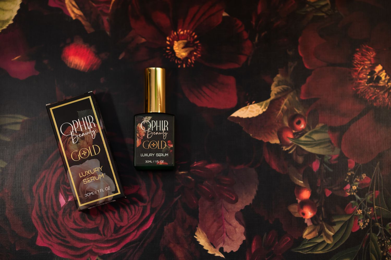 A bottle of Ophir Gold luxury serum lies on a rich floral background with its gilded retail box beside it.