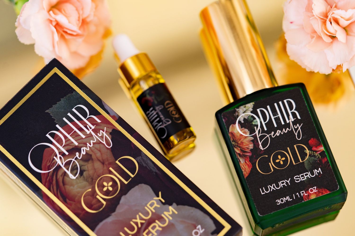 Ophir Gold luxury serum lies on a reflective gold surface with flowers beside