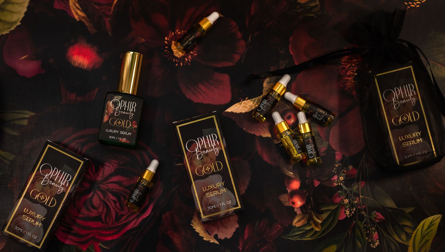 Ophir Gold luxury products are scattered across a rich floral surface