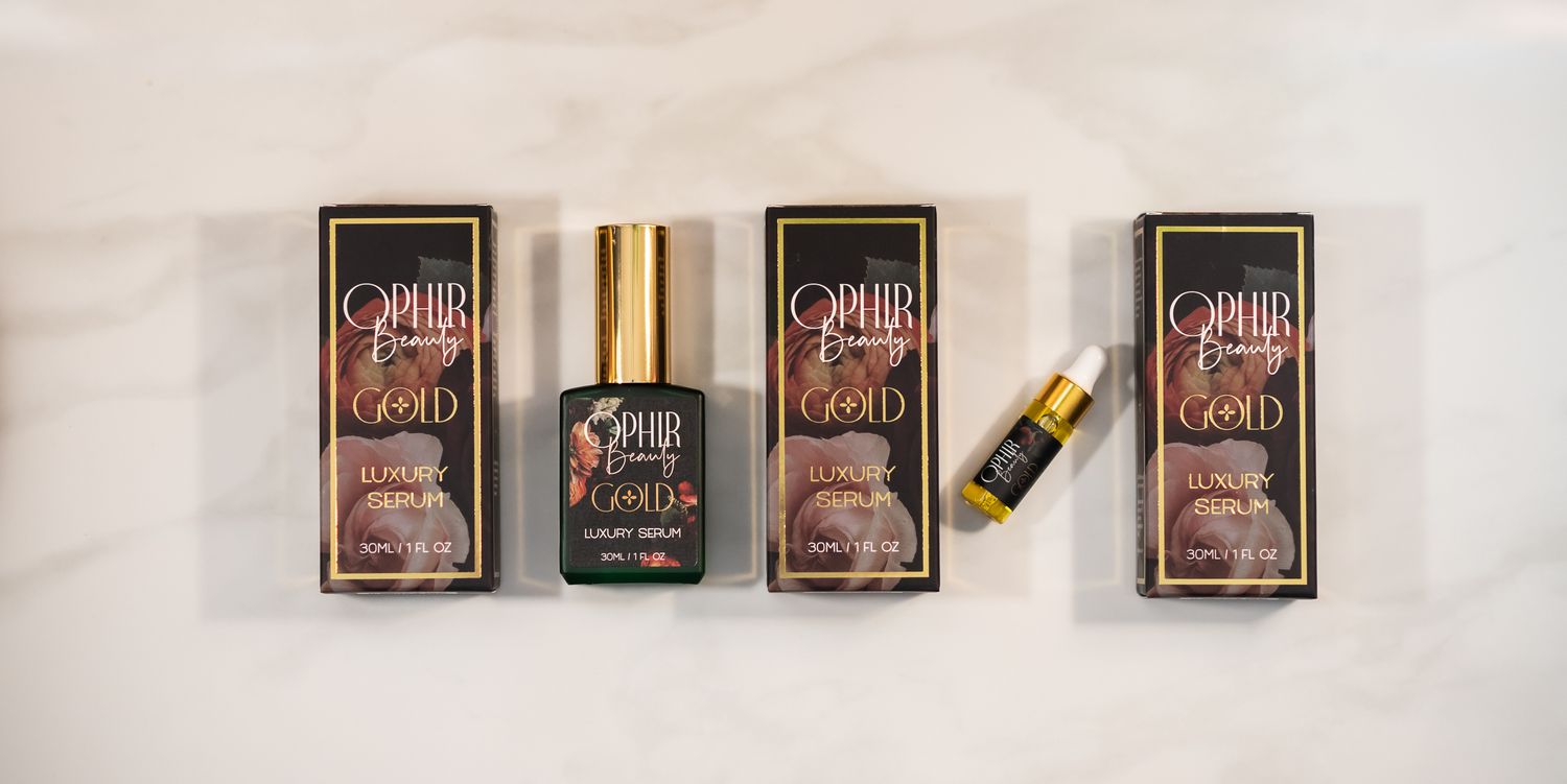 Ophir Beauty serums are lined up in a row, alternating with metallic gold and black floral Ophir retail boxes on a white marble background