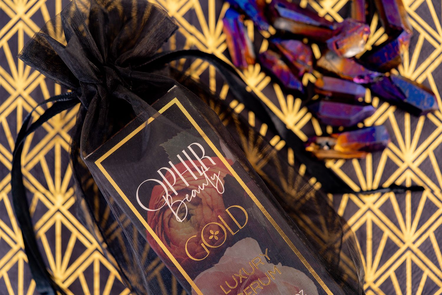 a boxed Ophir Gold serum in a black organza bag lies on a gold art deco patterned background