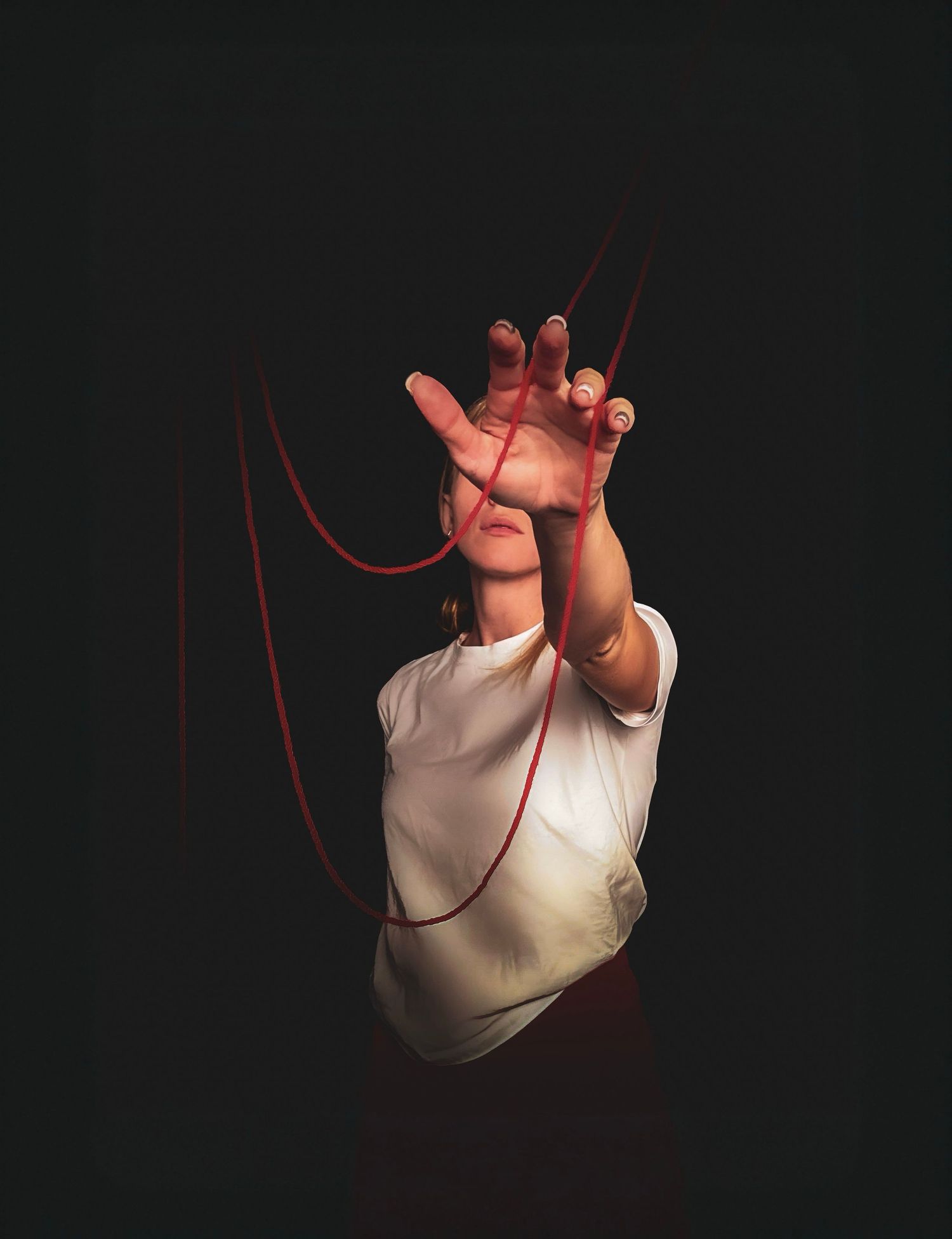 Person in a white t-shirt reaches a hand toward the camera, with red threads stretching through the dark, dramatic background.