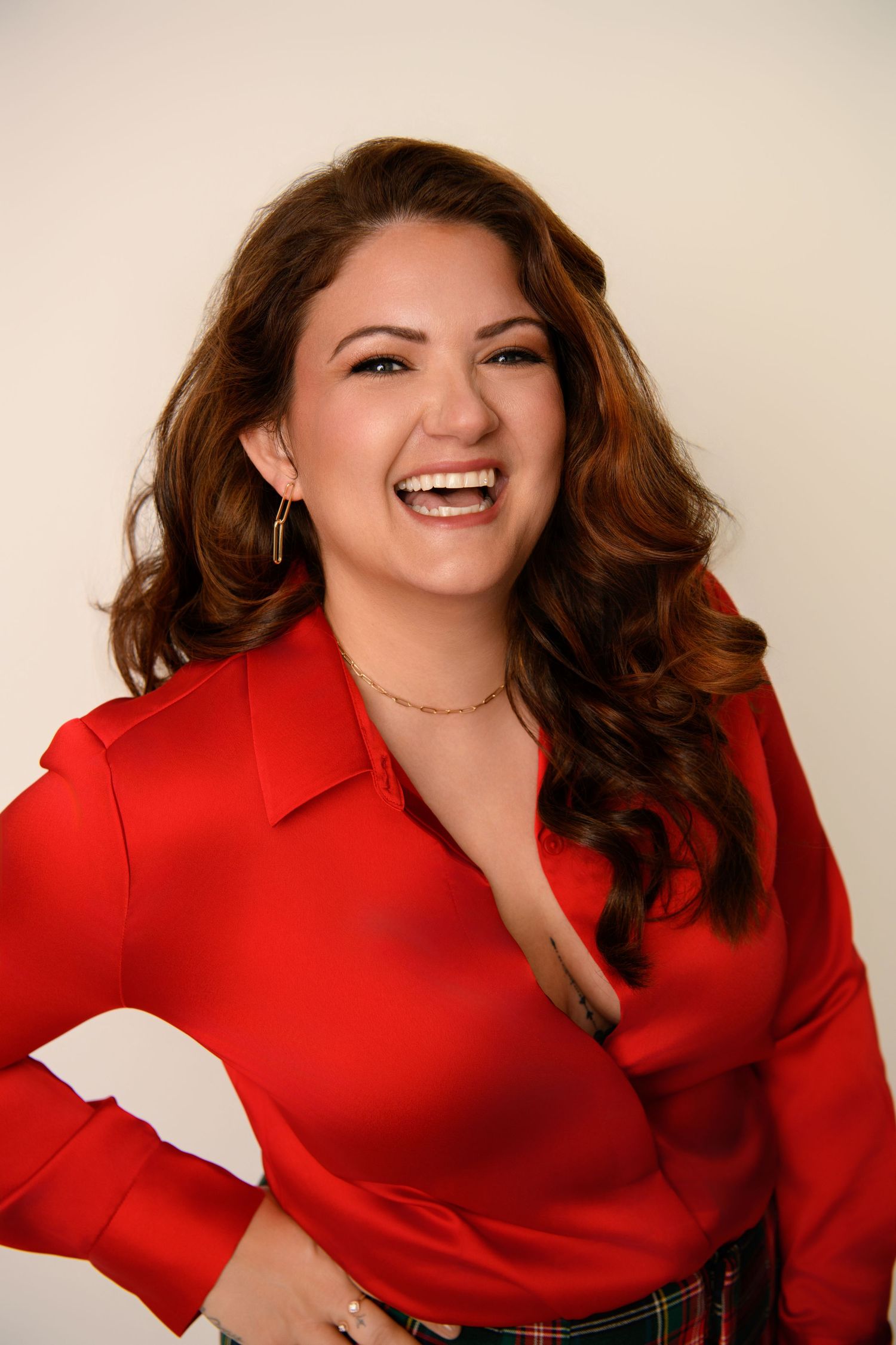 Smiling woman wearing a bright red top and statement earrings against a beige background.