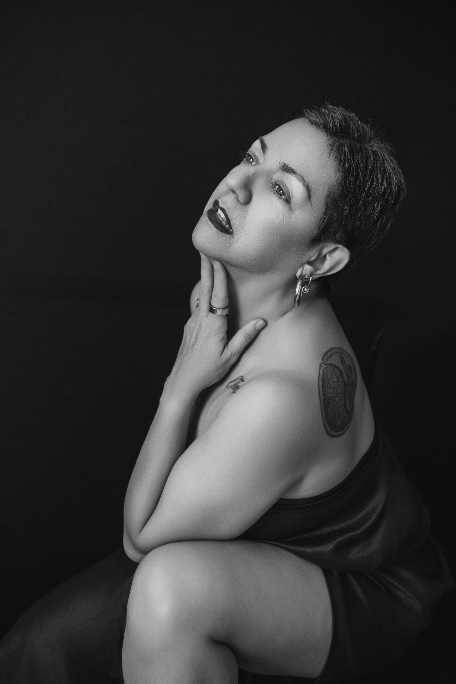 Dramatic monochrome portrait of a person with short hair posing against dark background.