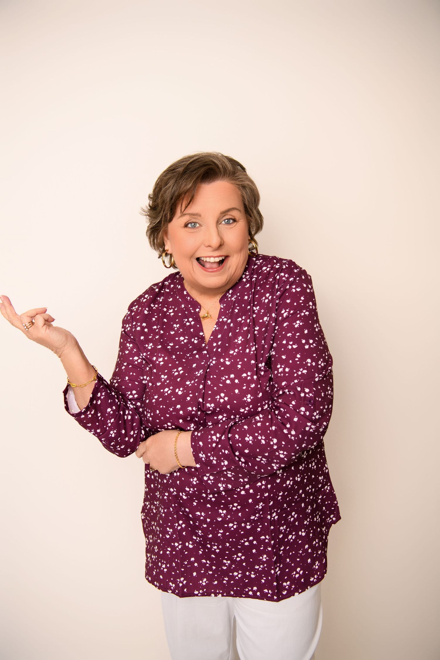 Energetic portrait in burgundy patterned top with animated expression against light background.