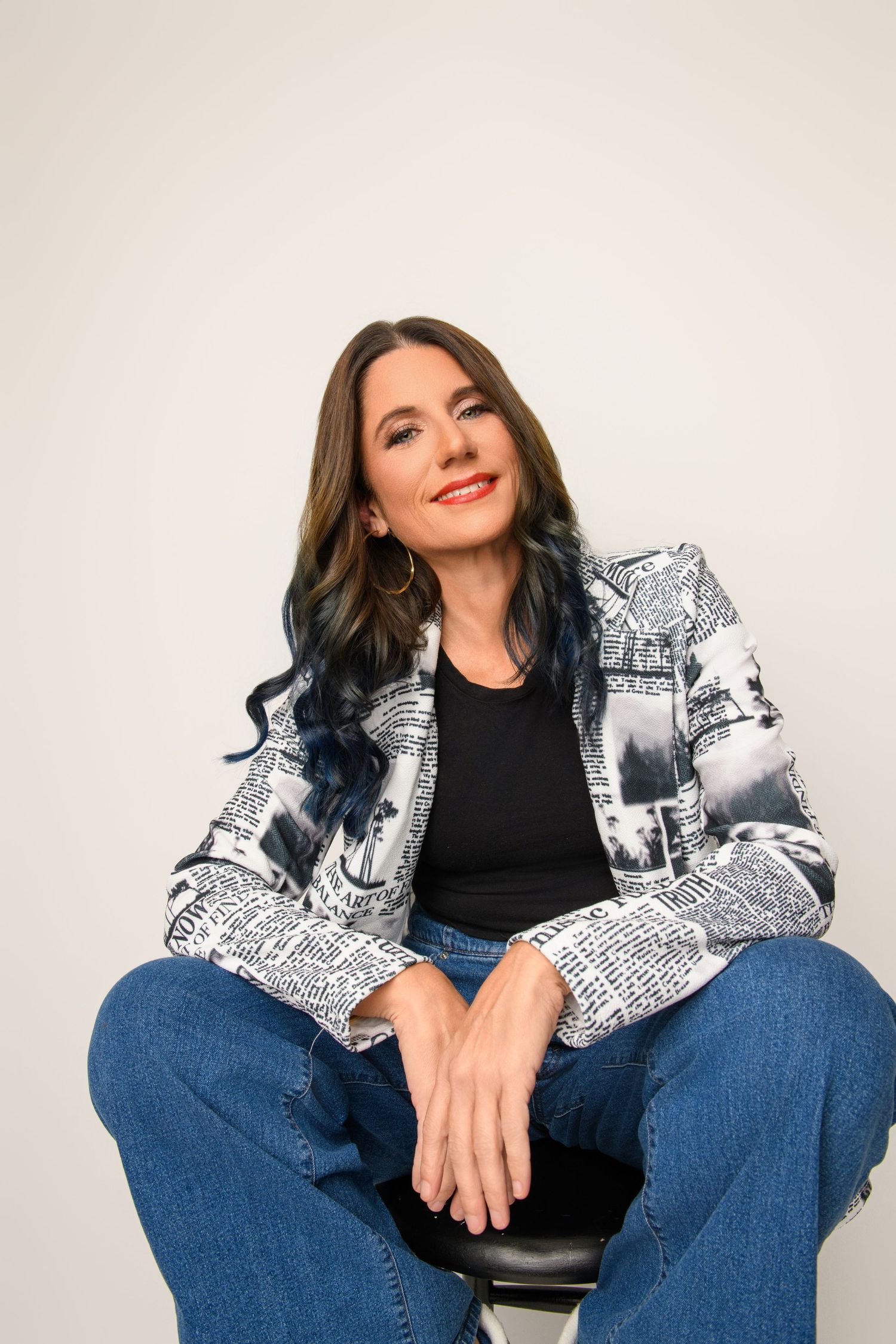 Casual portrait featuring newspaper print jacket and blue-tipped hair against white background.