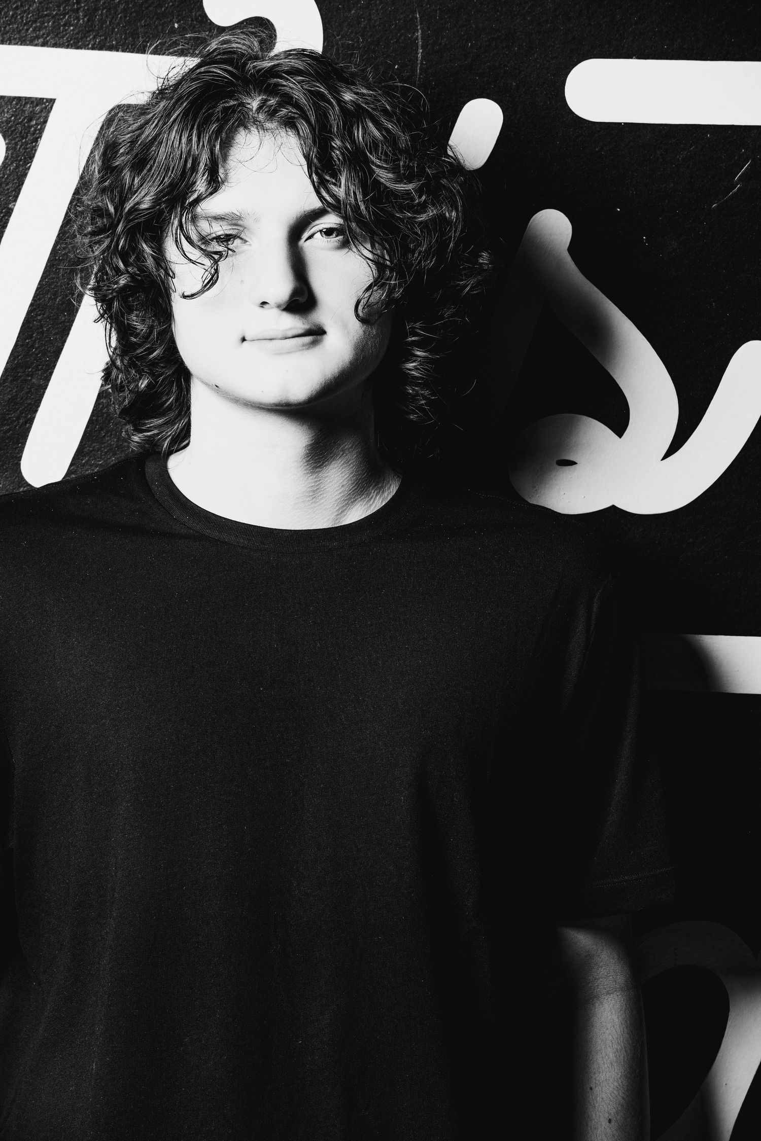 Black and white portrait of person in dark shirt against typographic wall art.