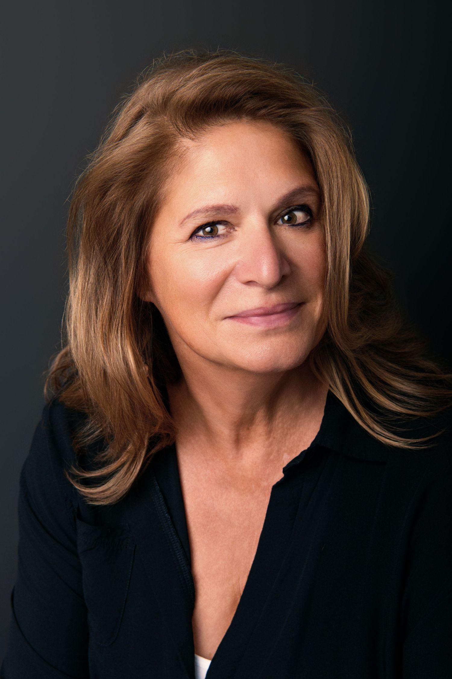 Studio headshot with warm lighting featuring black blazer and natural makeup.