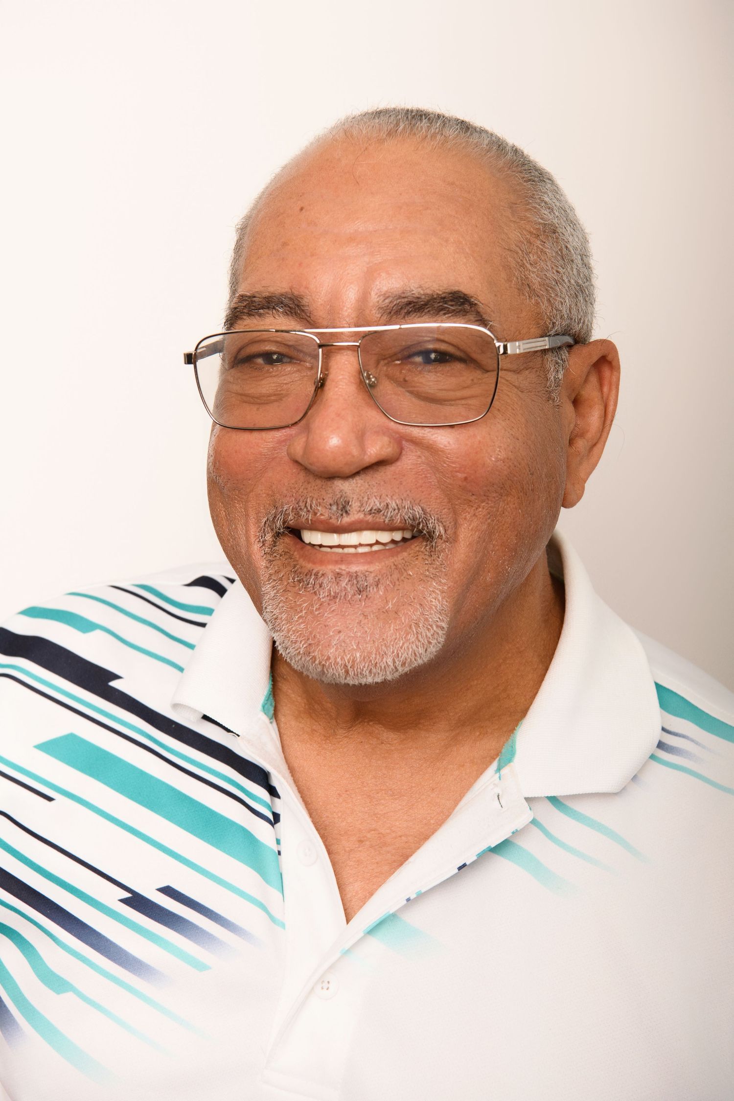 Cheerful senior wearing glasses and striped polo shirt against light background.