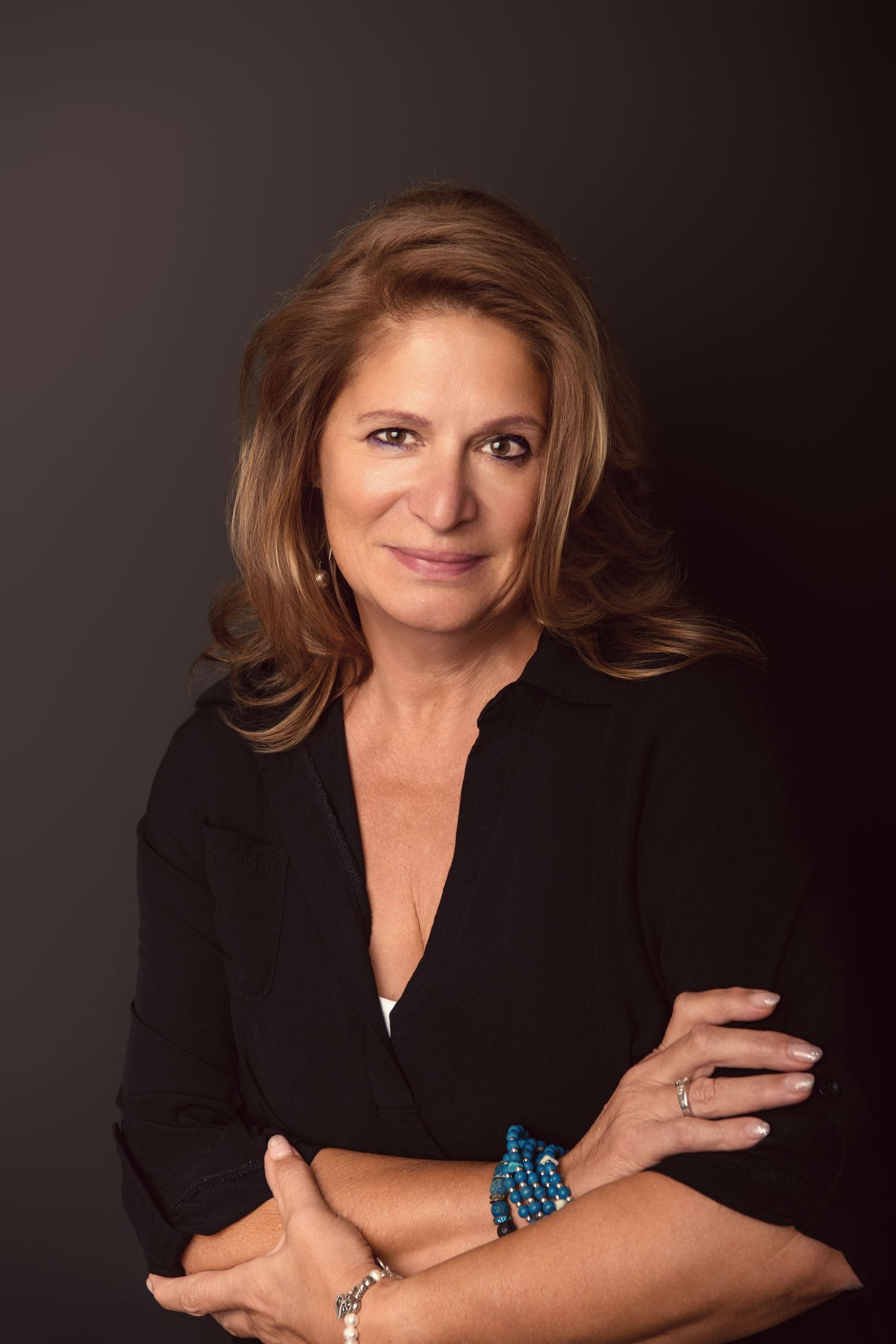 Professional portrait against dark background showing confident pose in black blazer with turquoise bracelet.