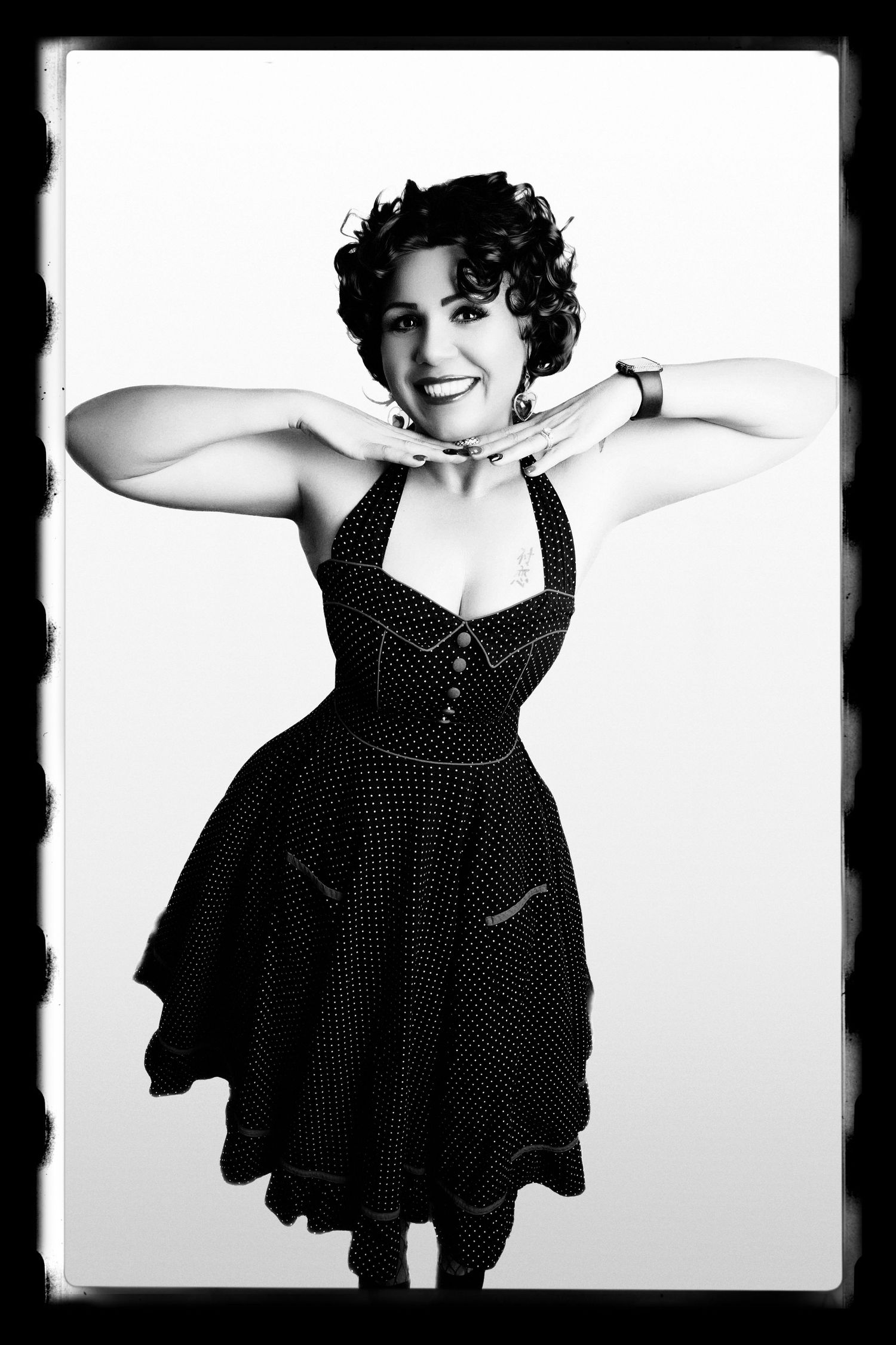Black and white portrait of woman in polka dot dress striking playful pose.