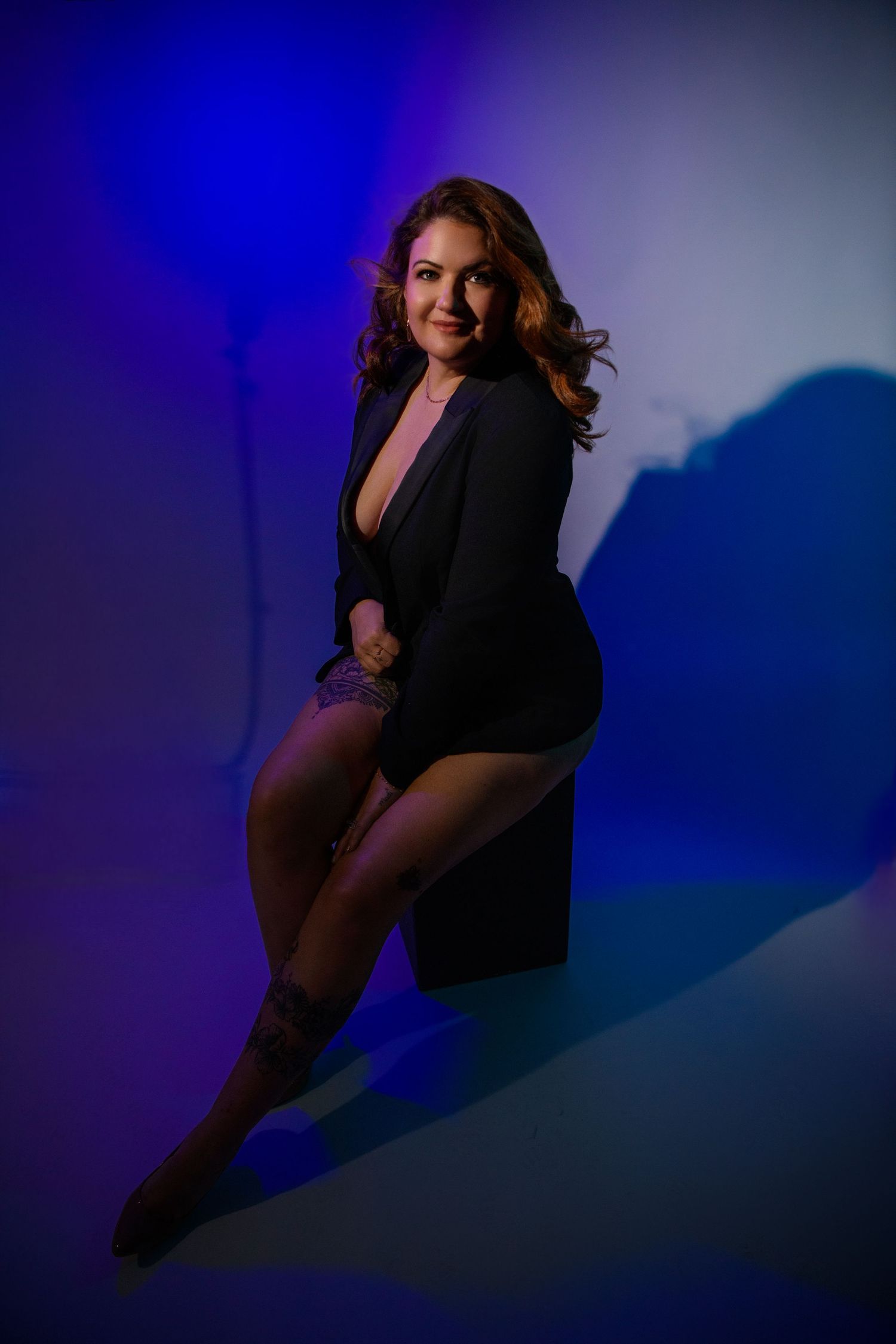 Dramatic studio portrait with vibrant blue lighting showing a figure in a black outfit against a colorful backdrop.
