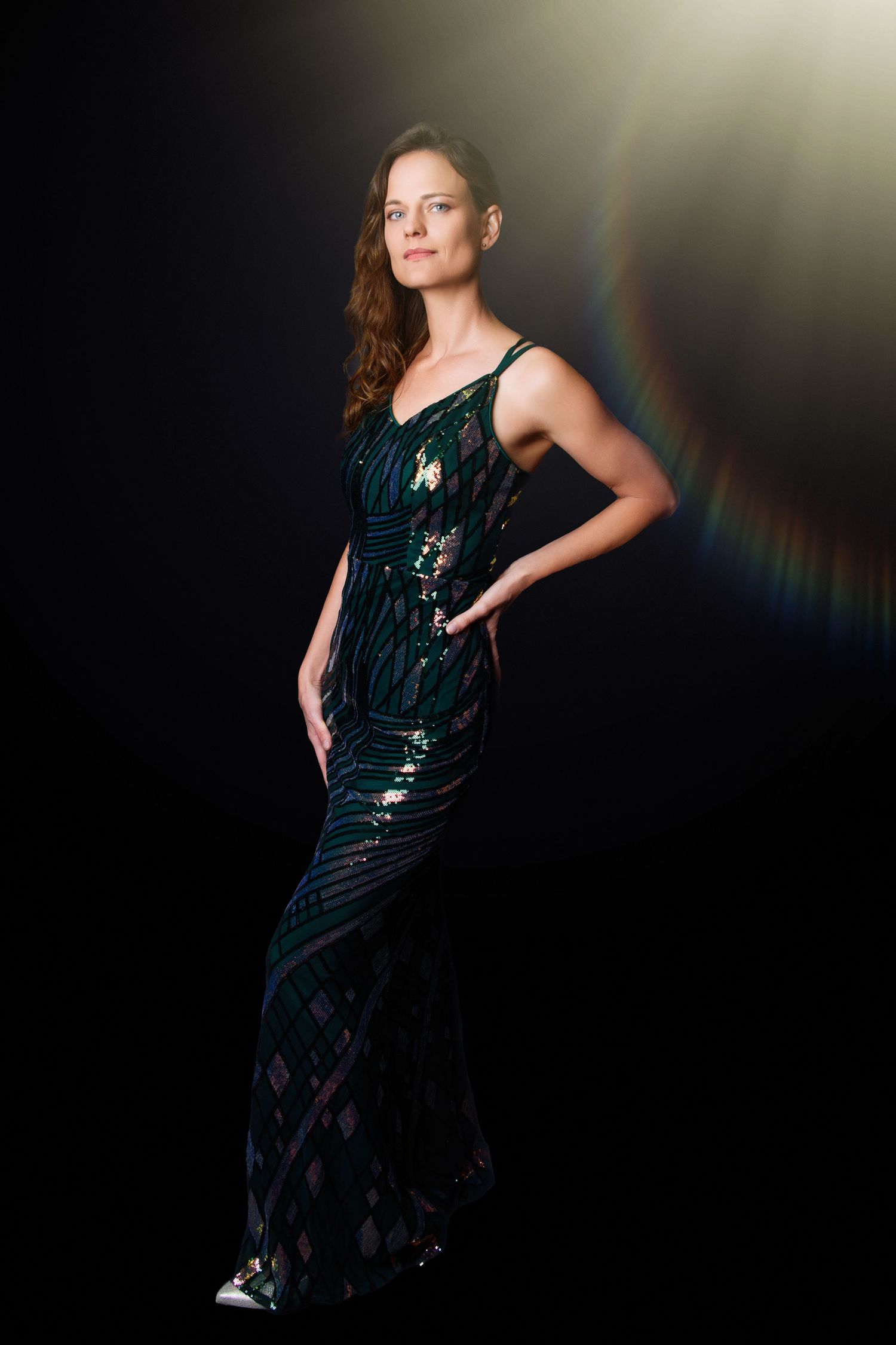 Model in sparkly evening gown poses dramatically with rainbow light effect.