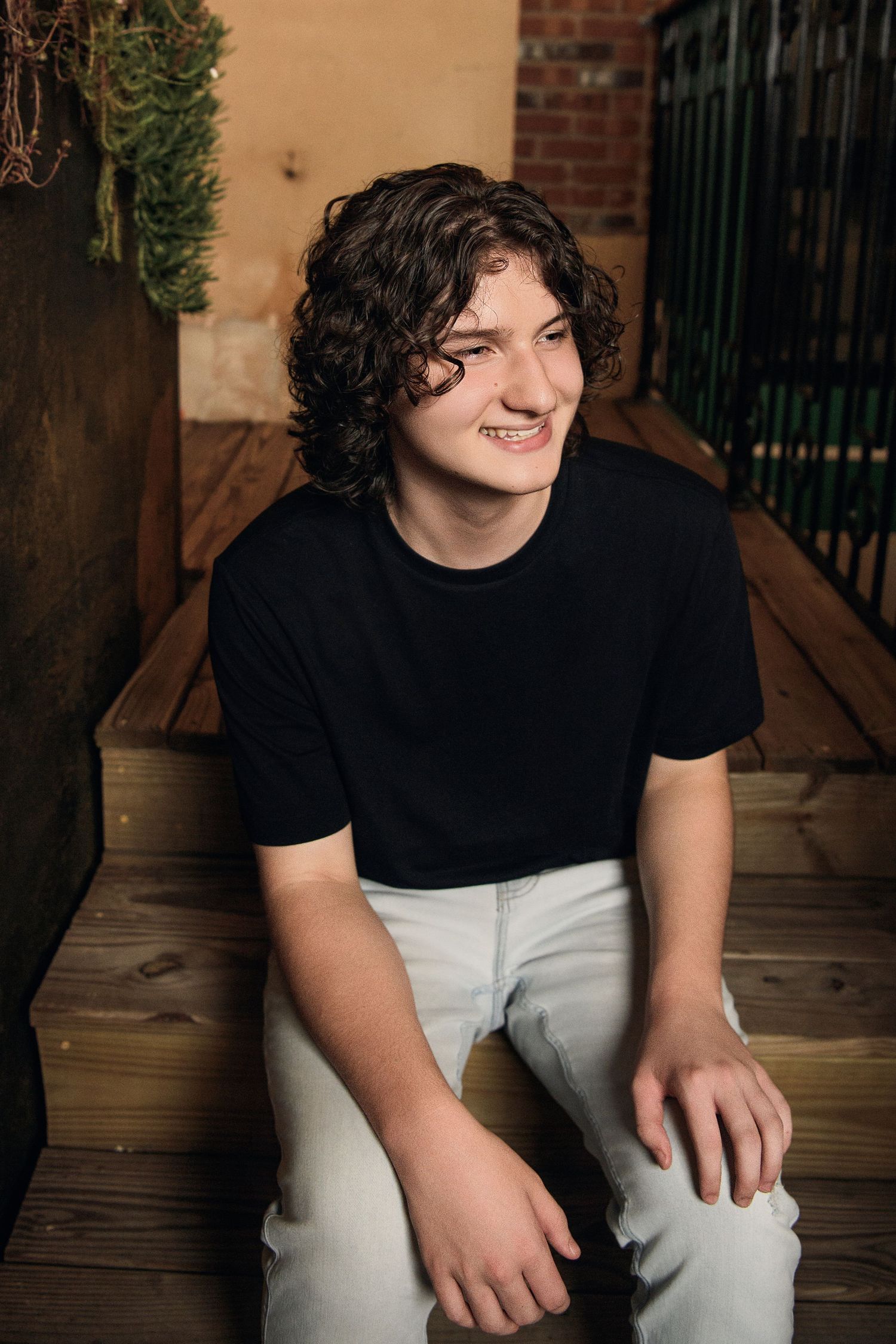 Casual outdoor portrait of person in black t-shirt sitting on wooden deck steps.