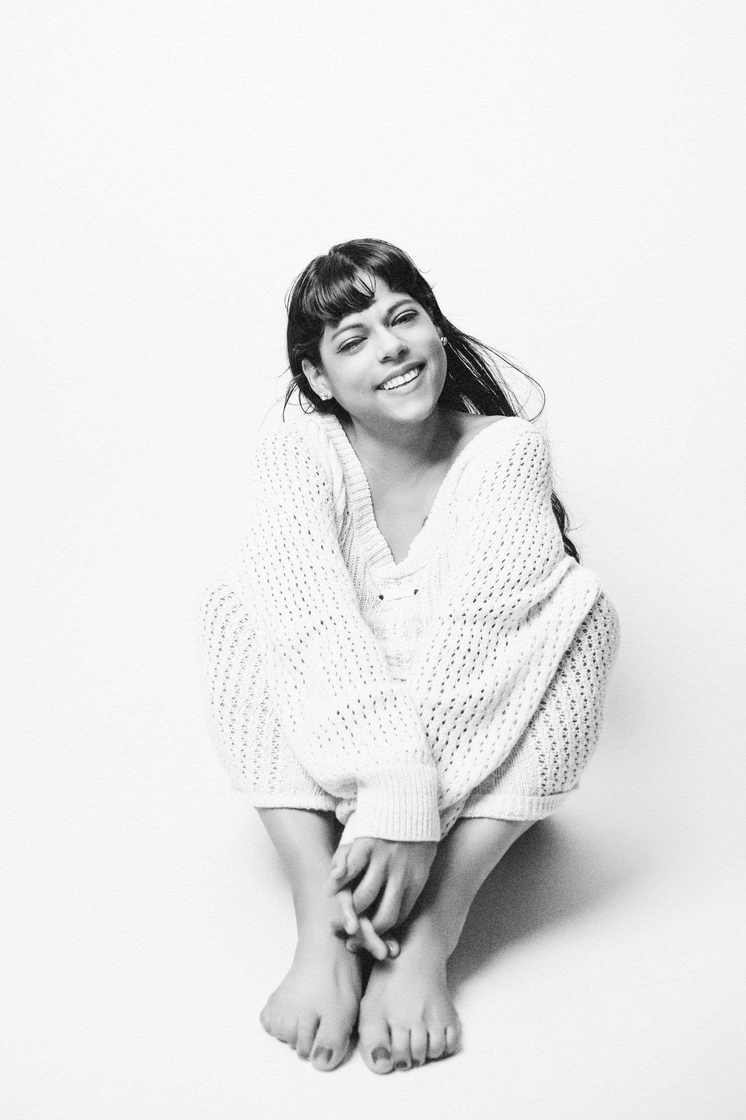Artistic black and white photo of a model in white knitwear sitting with bare feet.